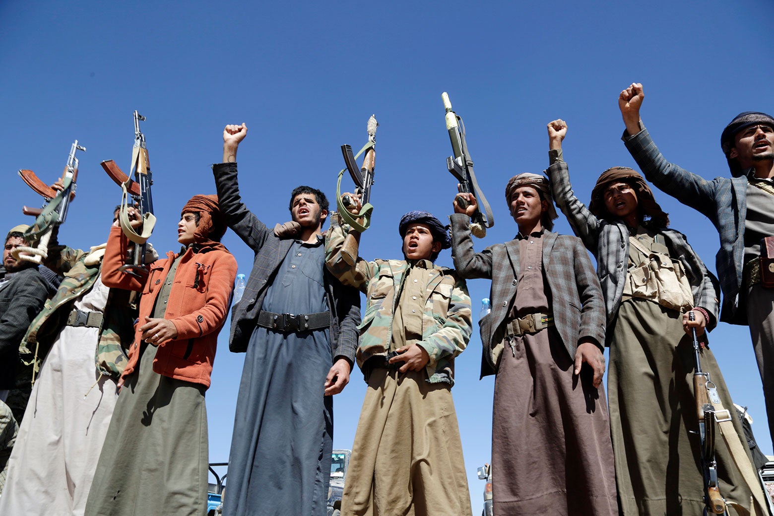 Men in traditional garb hold up rifles and shout.