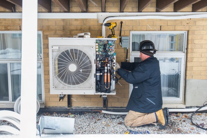 A worker installs a heat pump on an apartment building.