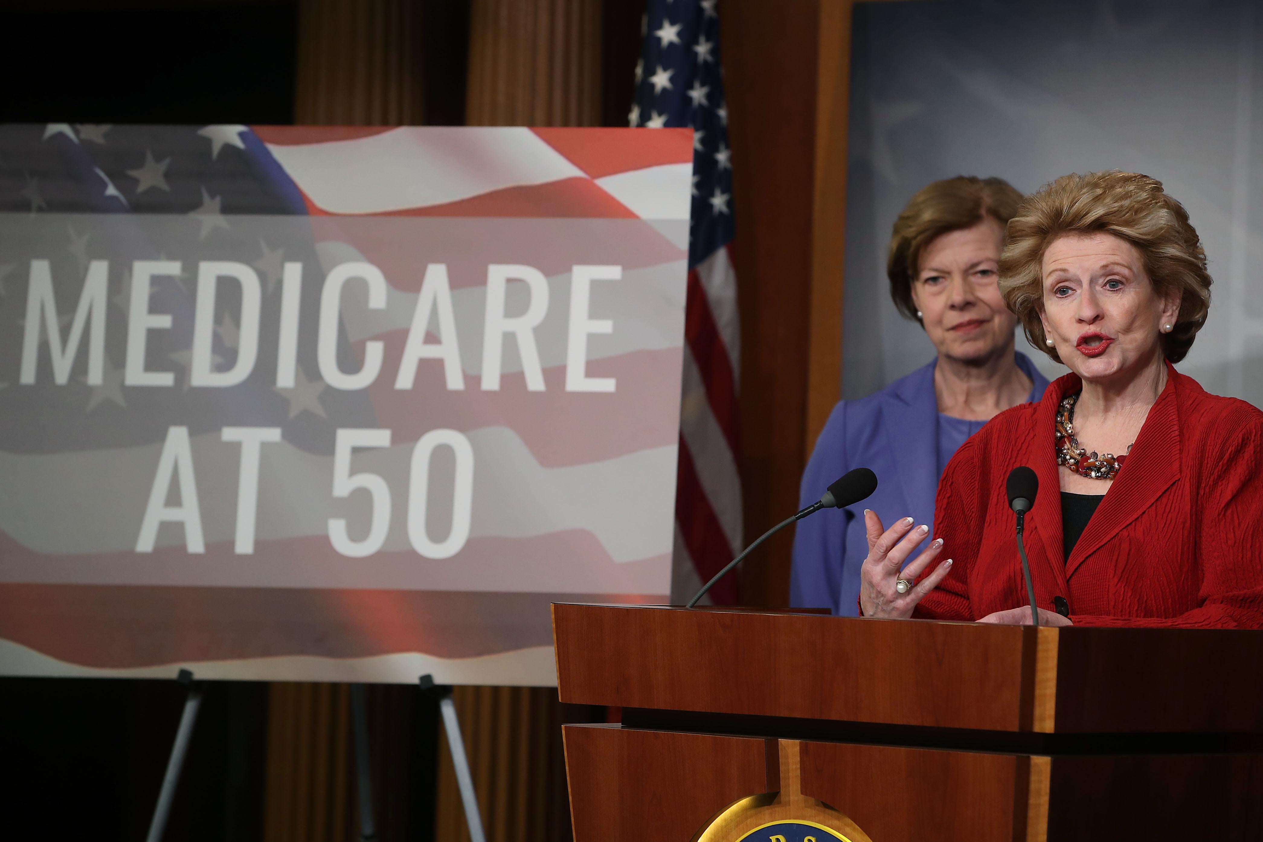 Tammy Baldwin and Debbie Stabenow onstage next to a poster reading "Medicare at 50."