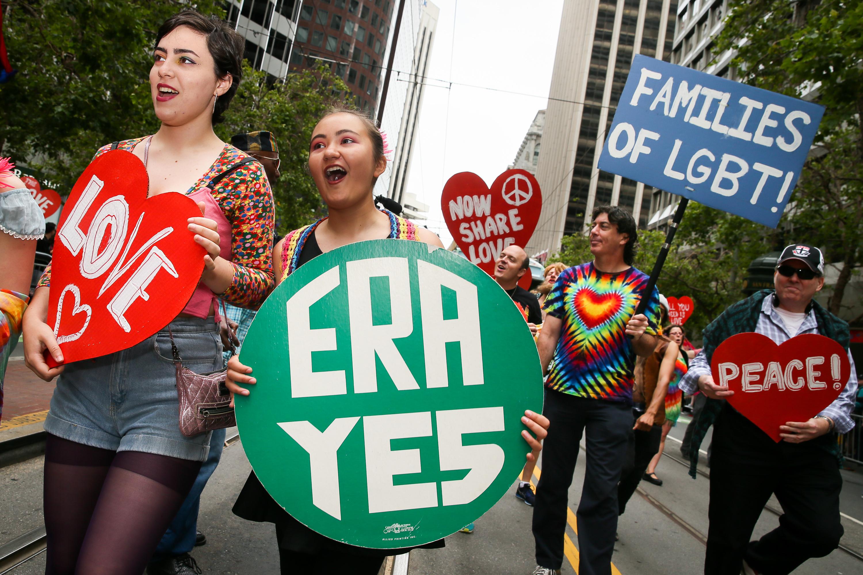 A marcher holds an "ERA YES" sign amid others holding pro-LGBTQ signs in the pride parade.