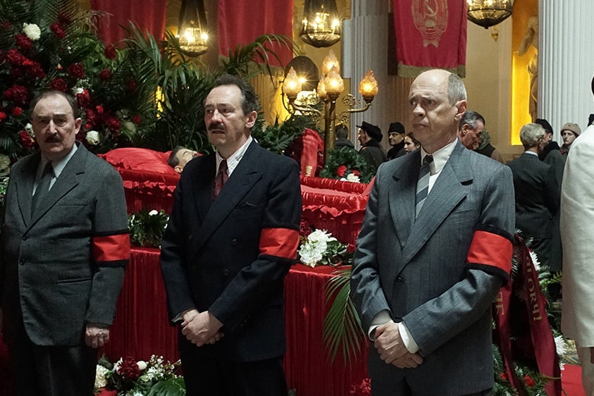 Dermot Crowley, Steve Buscemi, Jeffrey Tambor, and others stand around a casket.
