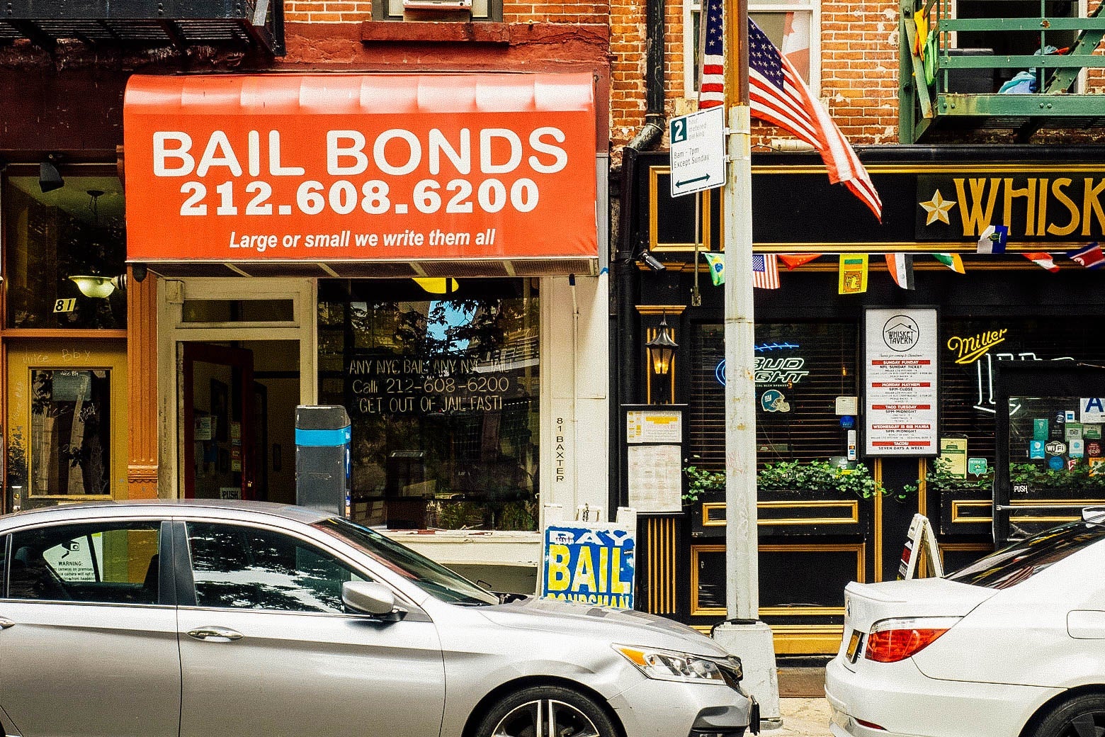 The storefront of a bail bonds shop with cars parked on the street in front of it in New York City.