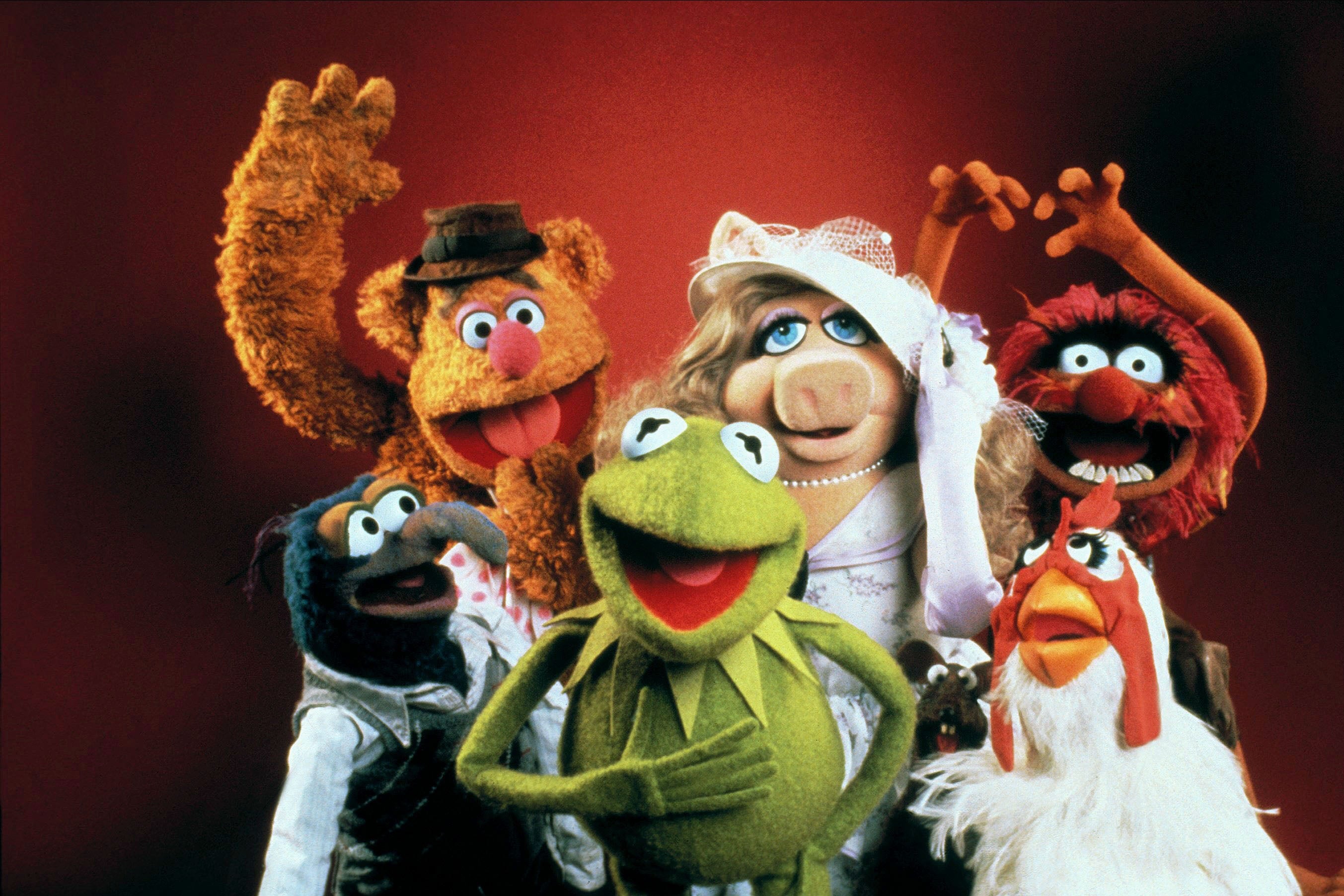 A collection of the Muppets pose happily against a red background.