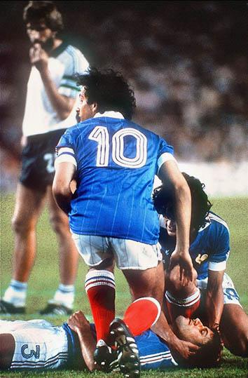French defender Patrick Battiston lies on the ground as midfielder Michel Platini (10) and forward Didier Six.