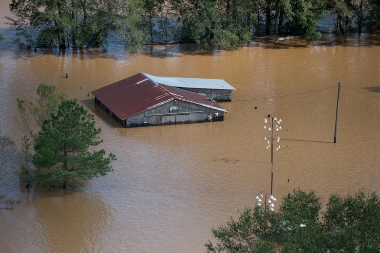 An aerial shot of a roof of a barn surrounded by brown flood waters