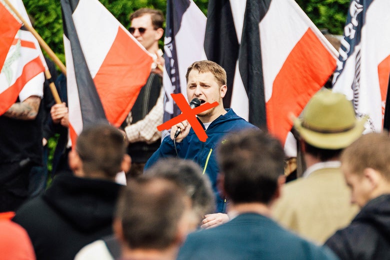 A neo-Nazi giving a speech at a rally, with an illustrated red X over his face.
