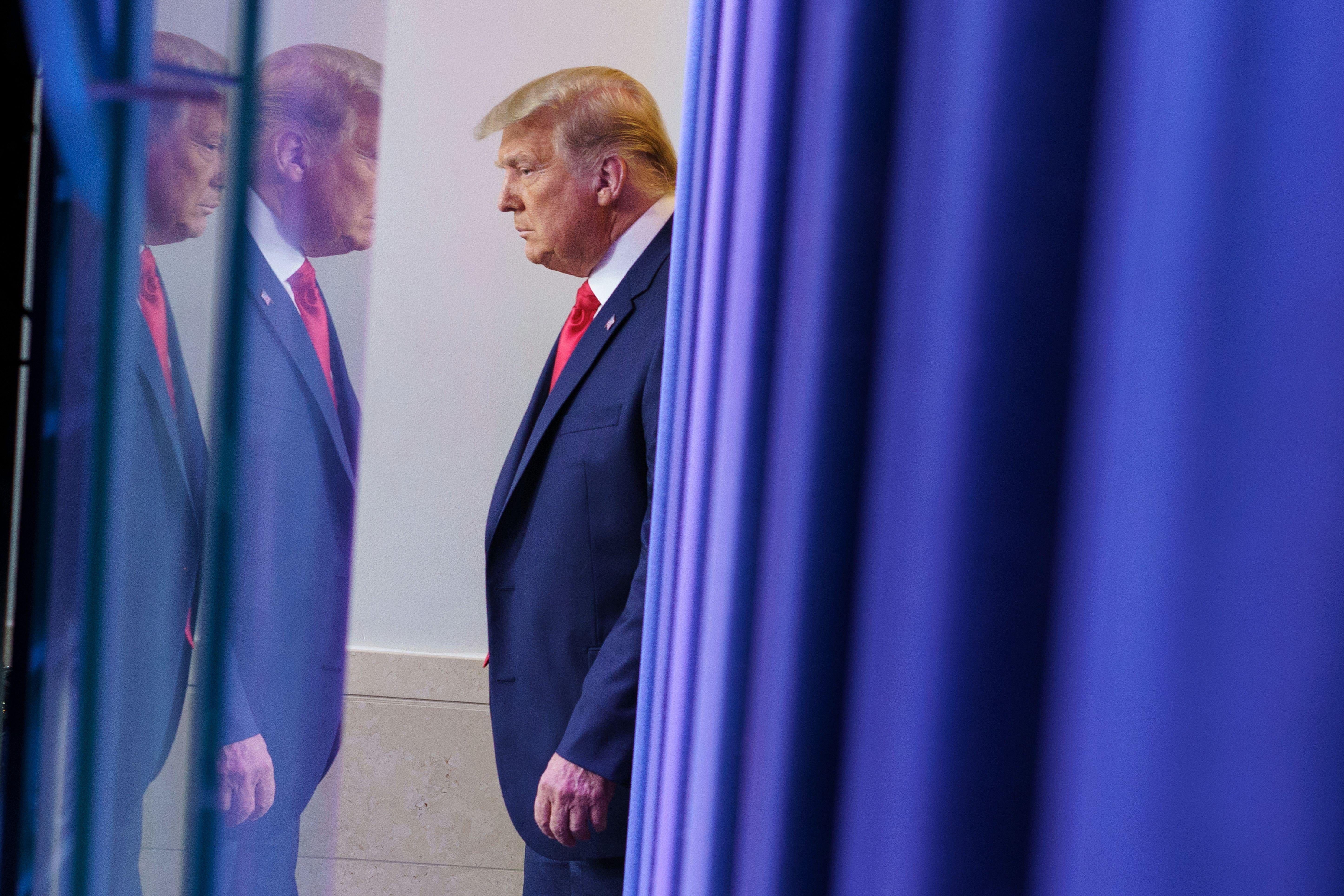 Trump appears depressed behind a curtain, his reflection showing.
