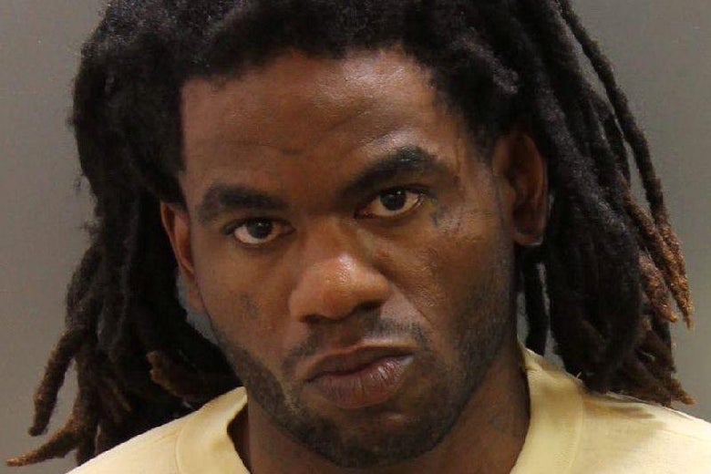 Booking photo of a man with dreadlocks and yellow shirt
