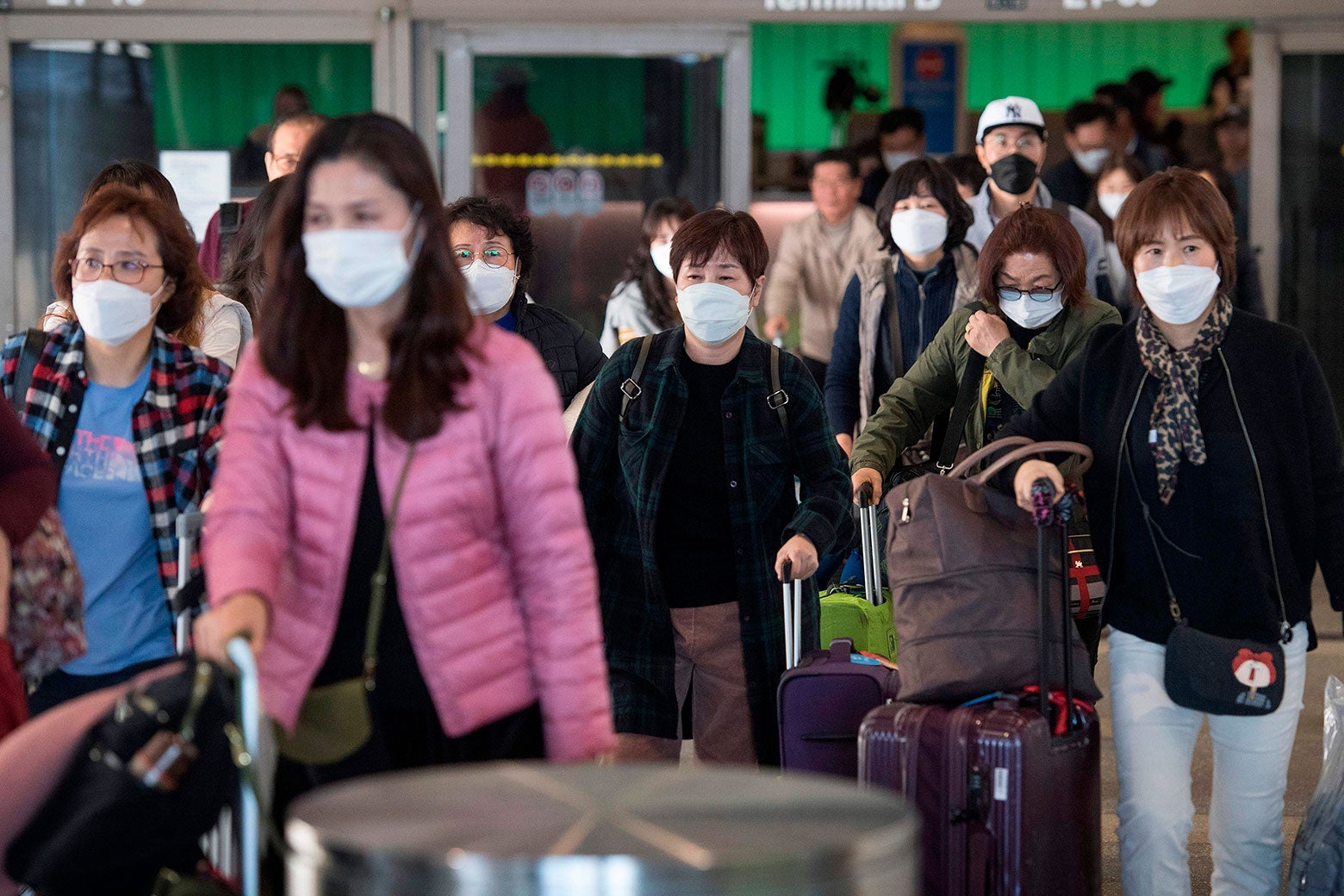 Airline passengers walk while carrying roller bags and wearing protective masks.