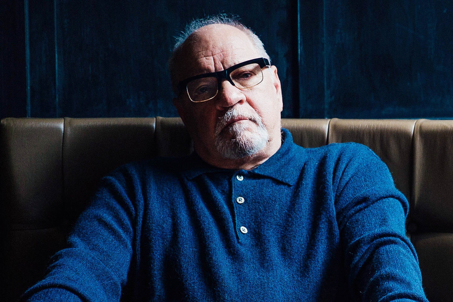 Paul Schrader in a blue shirt on a brown couch.