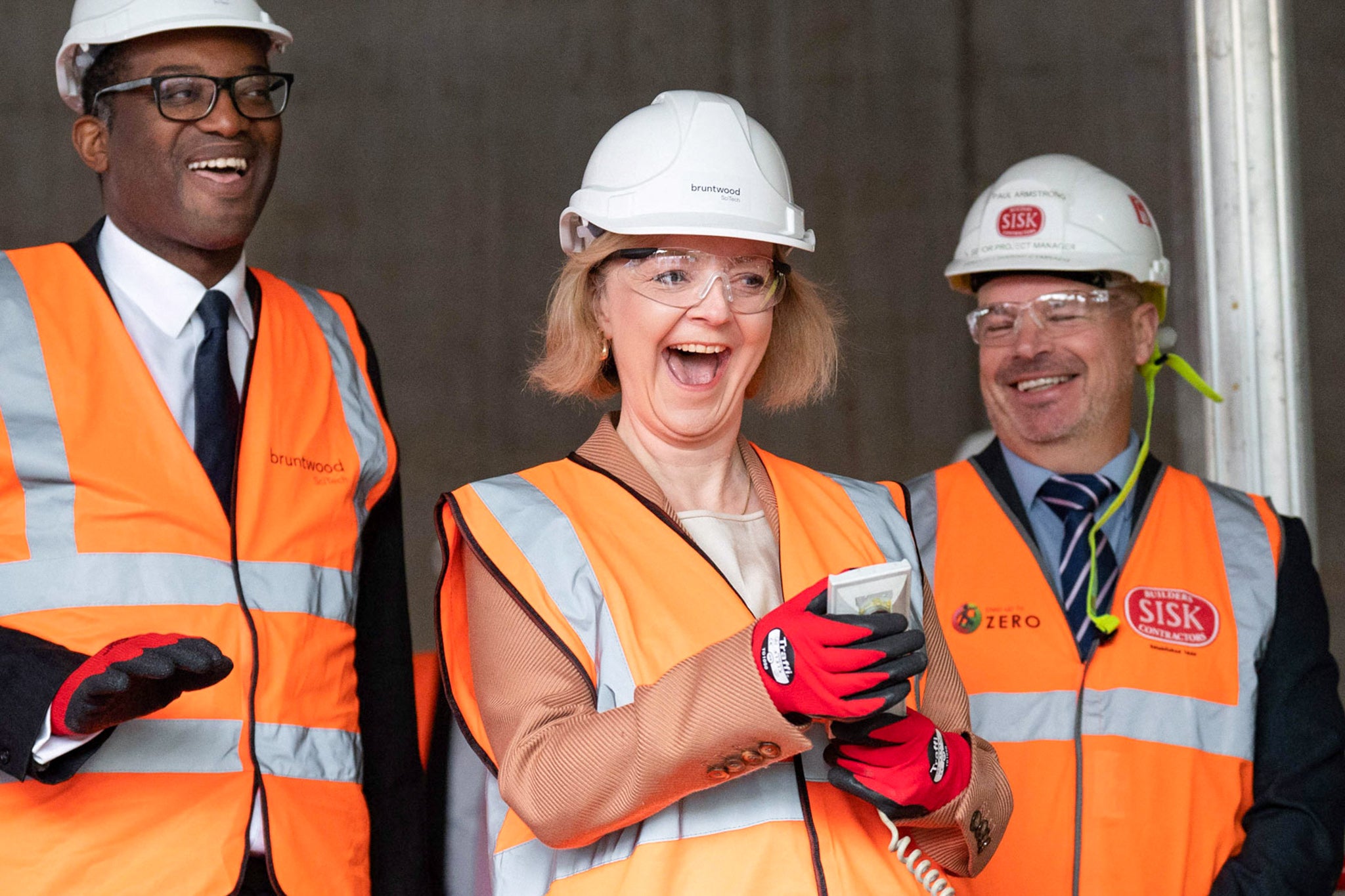 Britain's Prime Minister Liz Truss in an orange vest smiling wildly. 