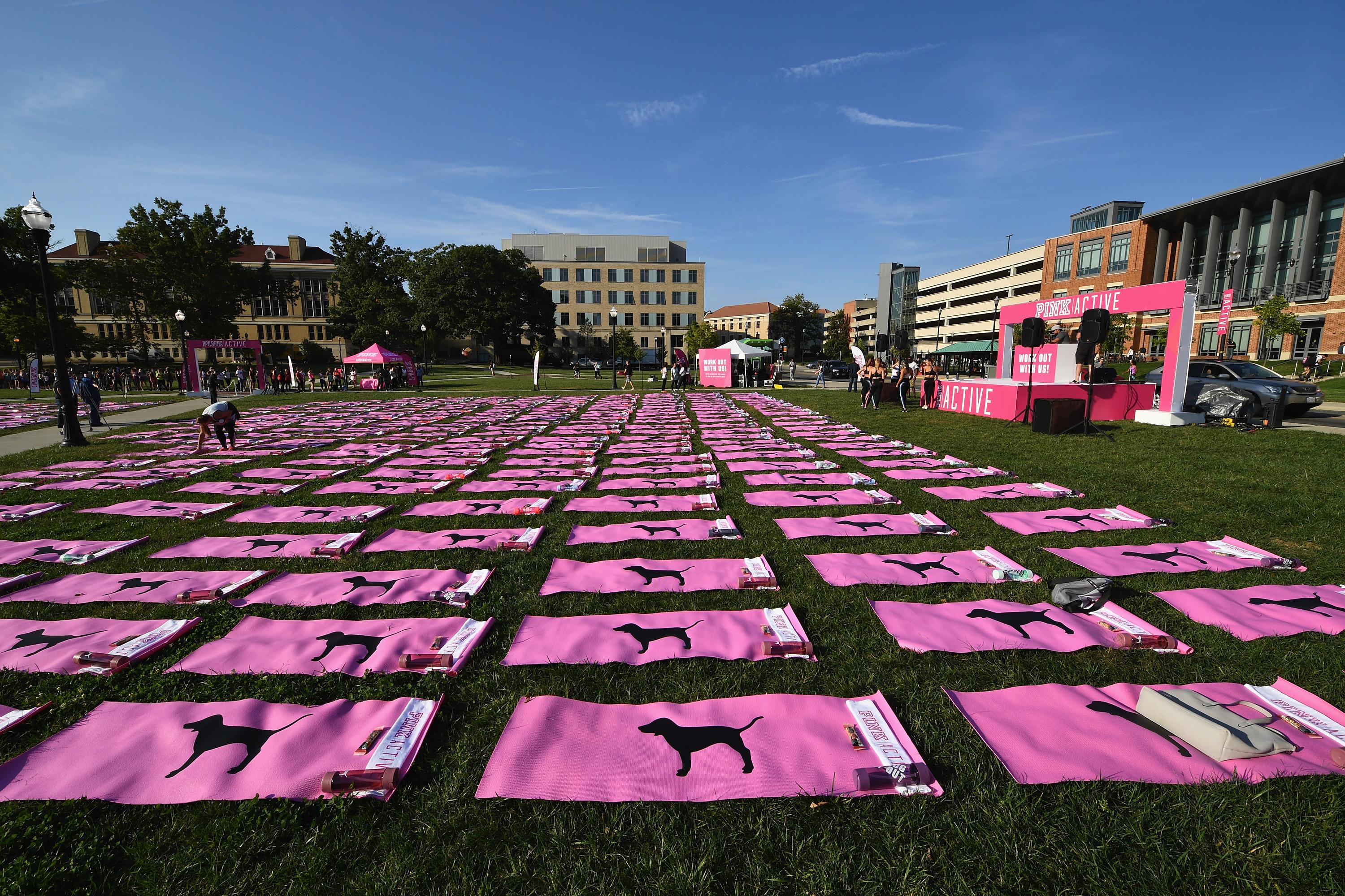 A view of the campus at Ohio State University, where Victoria's Secret's Pink held an event. A grassy field is covered in pink yoga mats, and there is a pink stage at the front of the field. 