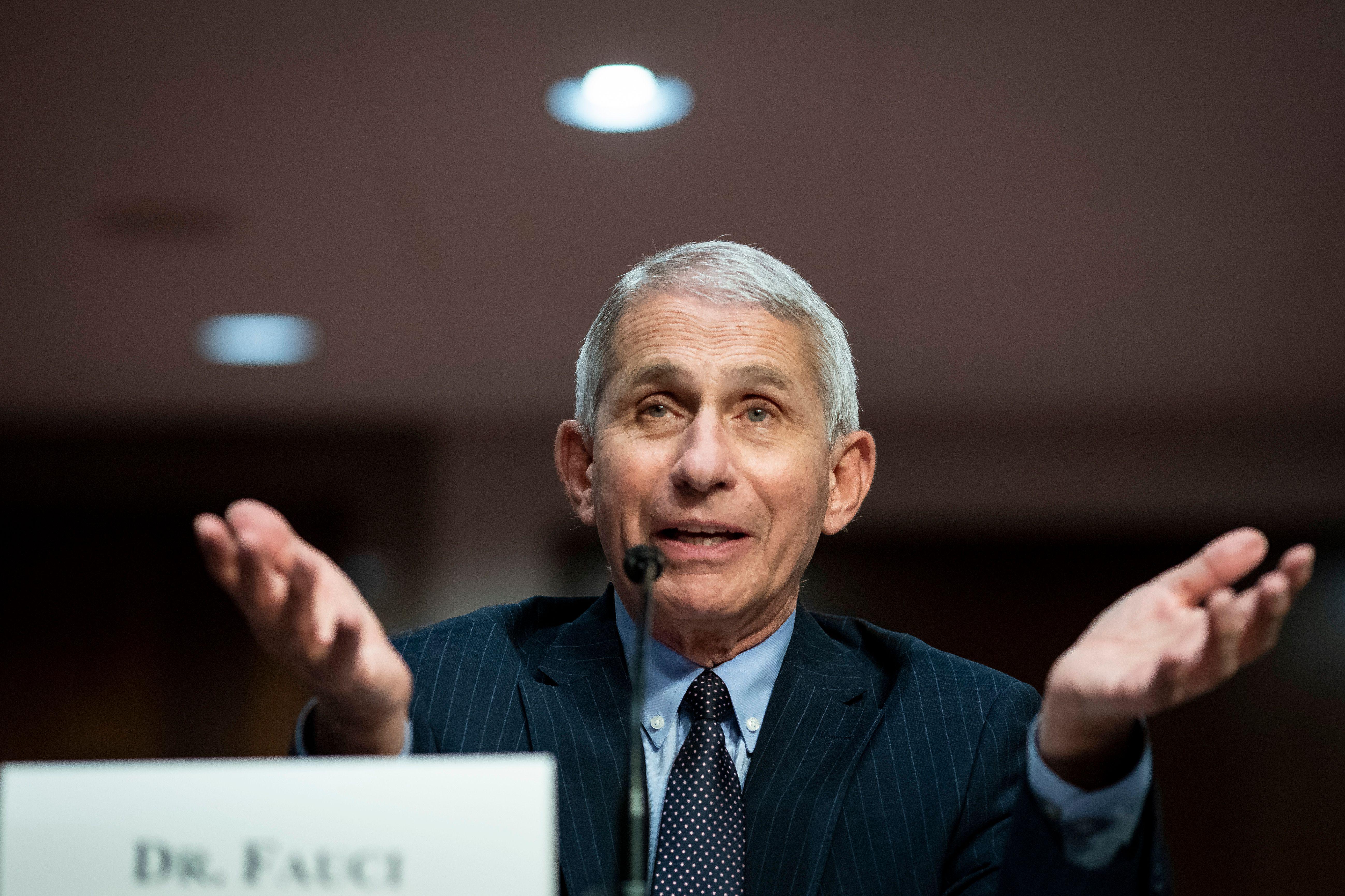 Fauci gestures while speaking at a mic
