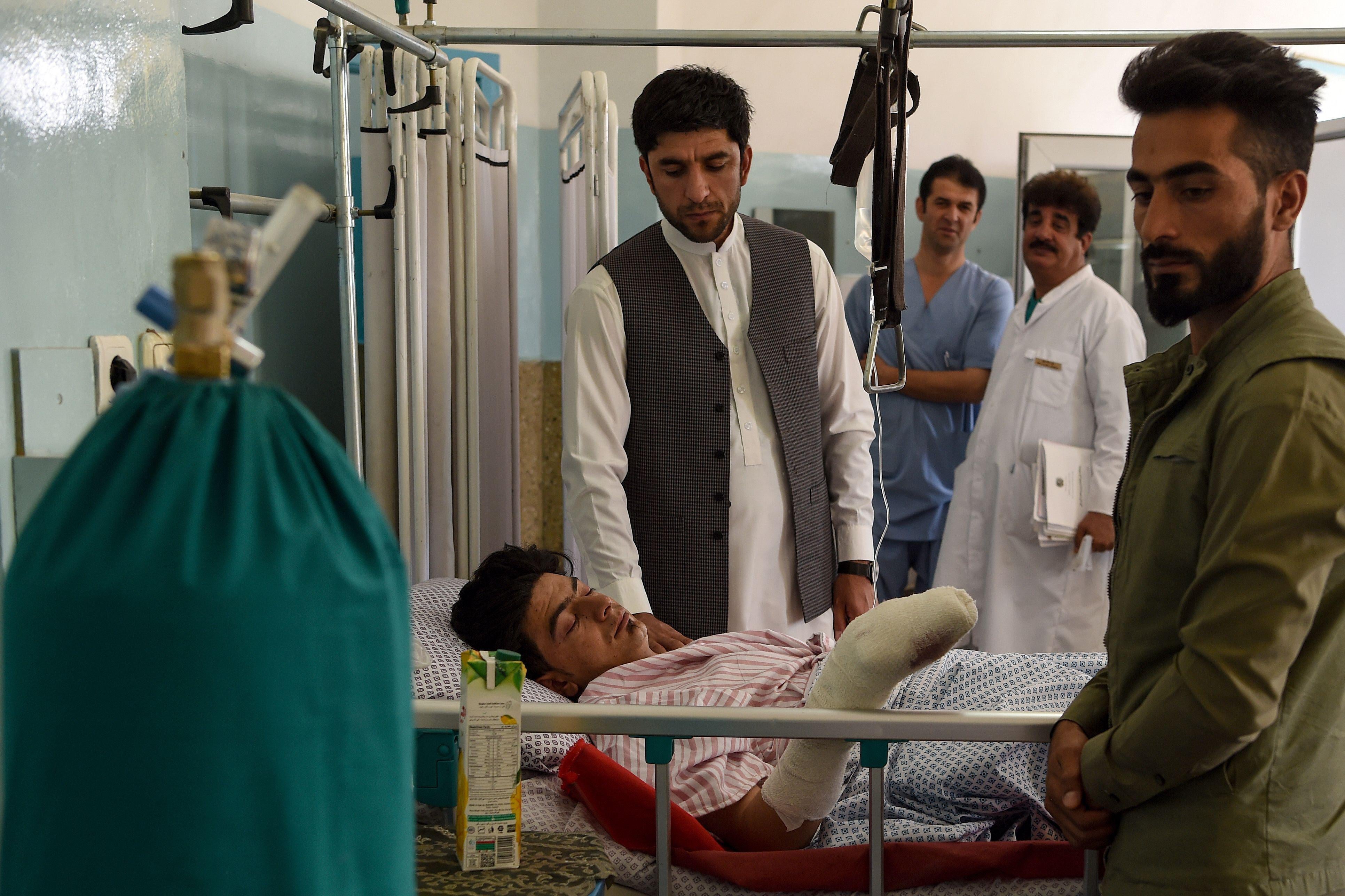 A wounded man receives treatment as people gather around him at the Wazir Akbar Khan hospital after a deadly bomb blast in a wedding hall in Kabul on August 18, 2019. 