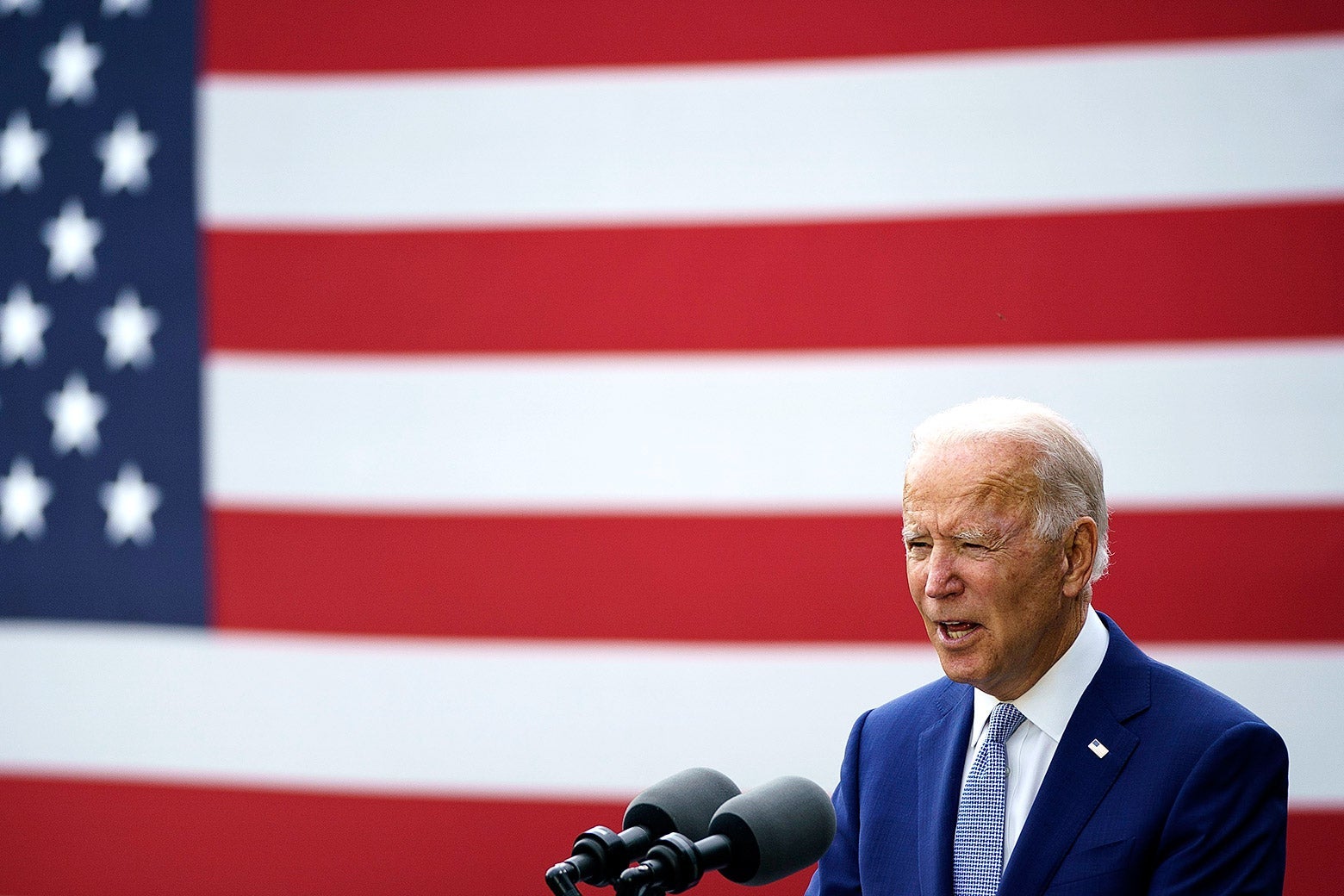 Joe Biden speaks into two microphones while standing in front of a U.S. flag.