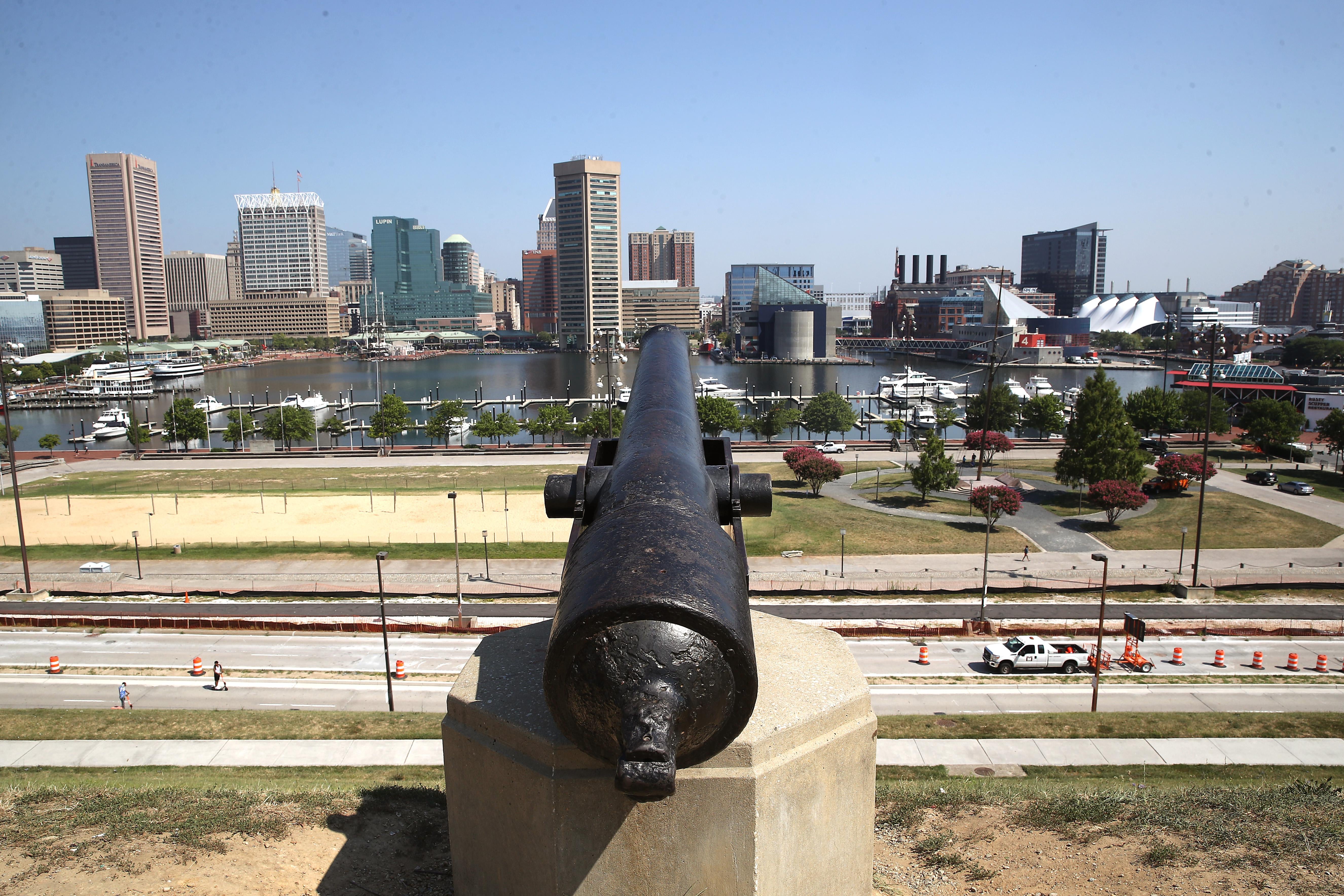 A cannon pointed at the Baltimore skyline on a sunny, cloudless day