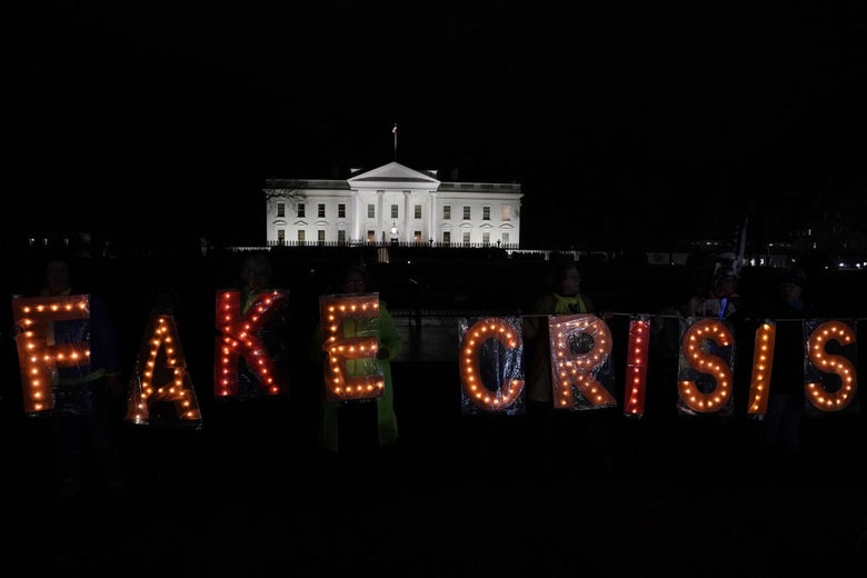 Protesters by the White House fence hold illuminated letters spelling out the words FAKE CRISIS.