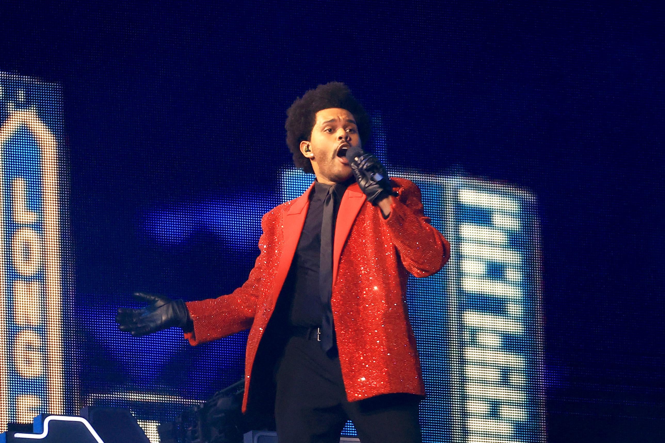 The Weeknd, in a red jacket and black suit, singing into a microphone at the Super Bowl.