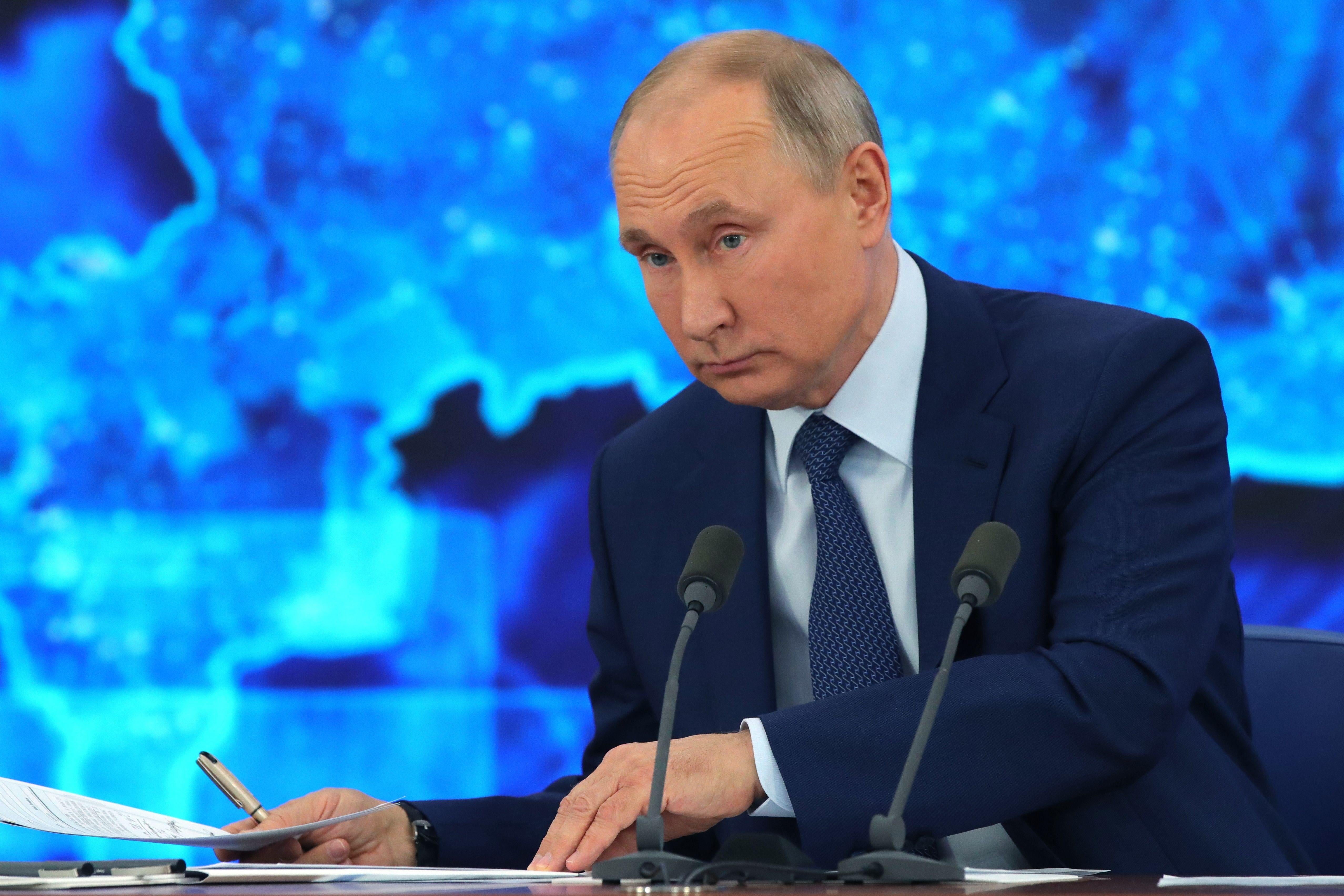 Putin at a desk, shuffling around papers.