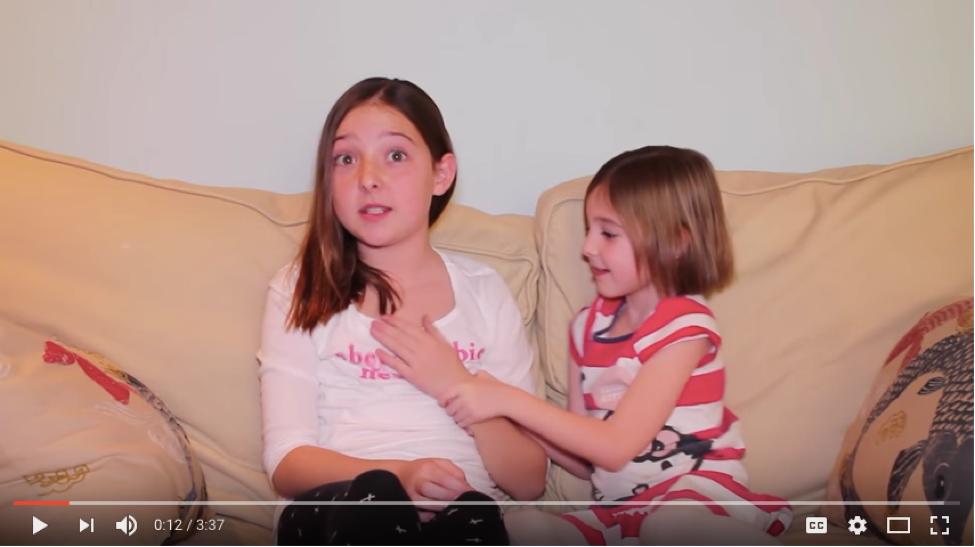 Screen capture from YouTube showing an older sister sitting on a sofa with a younger sister.