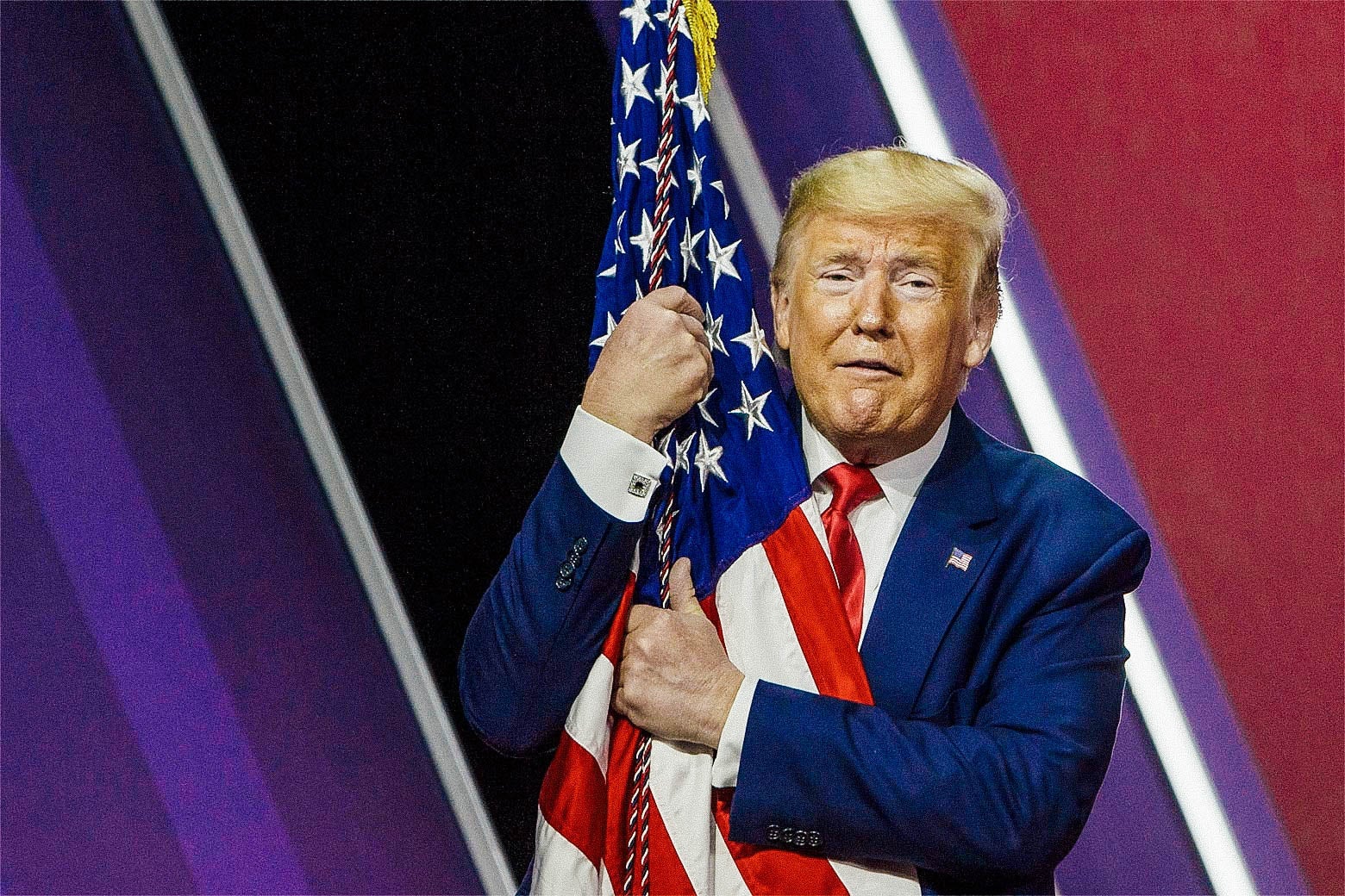Trump makes a funny face while wrapping his arms around an American flag.