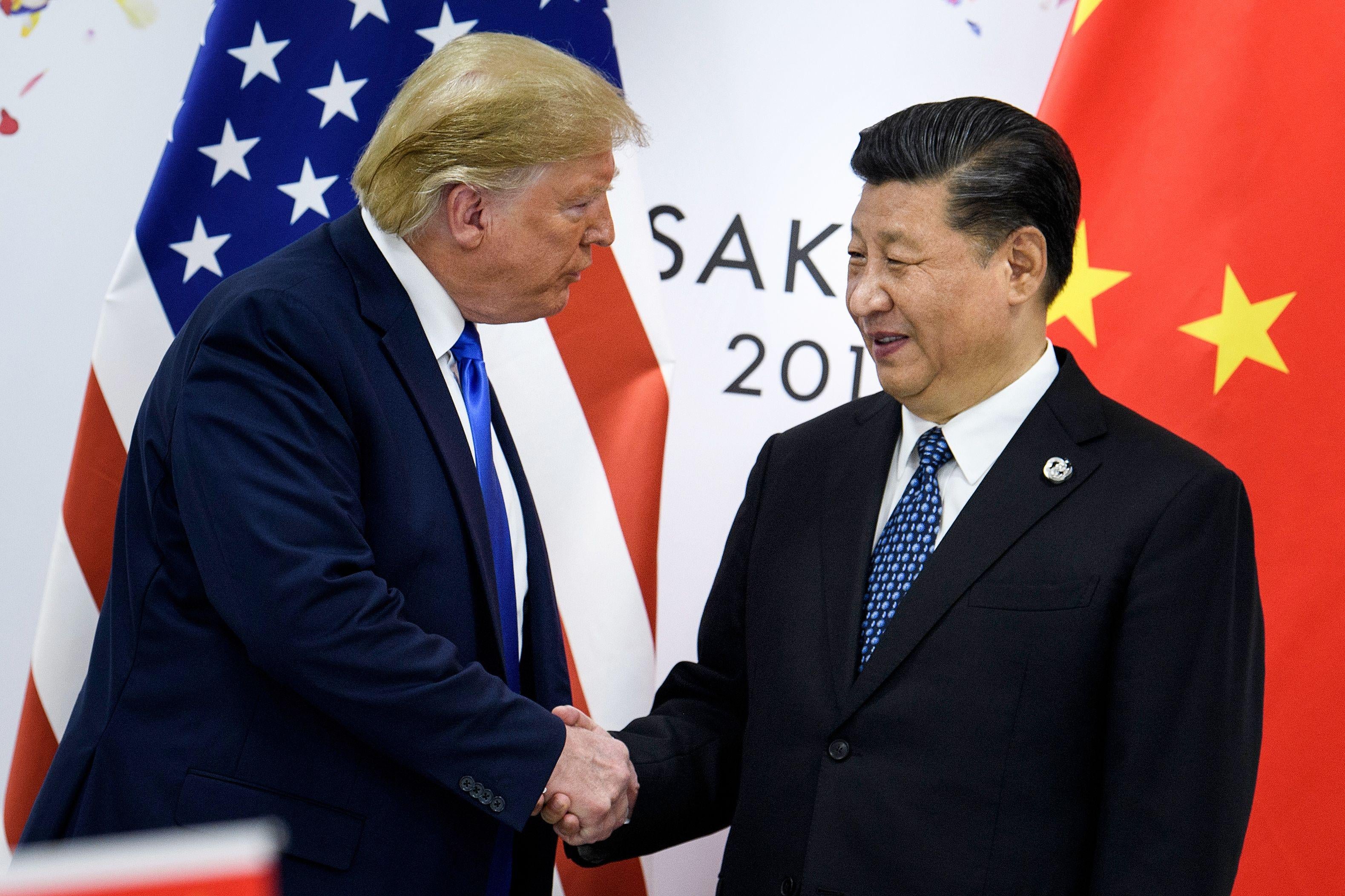 Donald Trump shakes hands with Xi Jinping in front of American and Chinese flags.