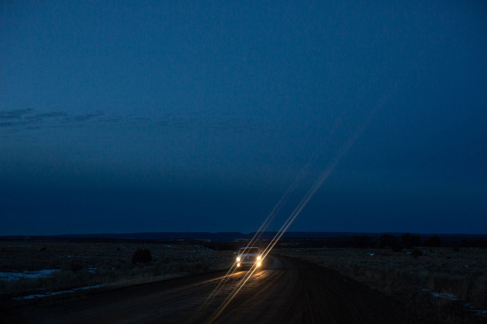 A truck drives down a road in low light with its headlines on.