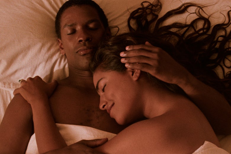 A shirtless Denzel Washington snuggles with Sarita Choudhury in bed.