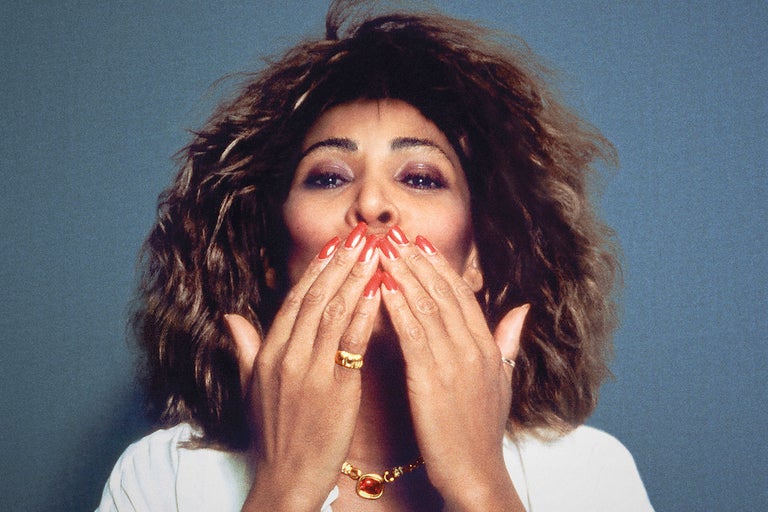 A photo of Tina Turner shows her looking at the camera, her hair all feathered out, both hands raised to her mouth, appearing to blow a kiss at the camera