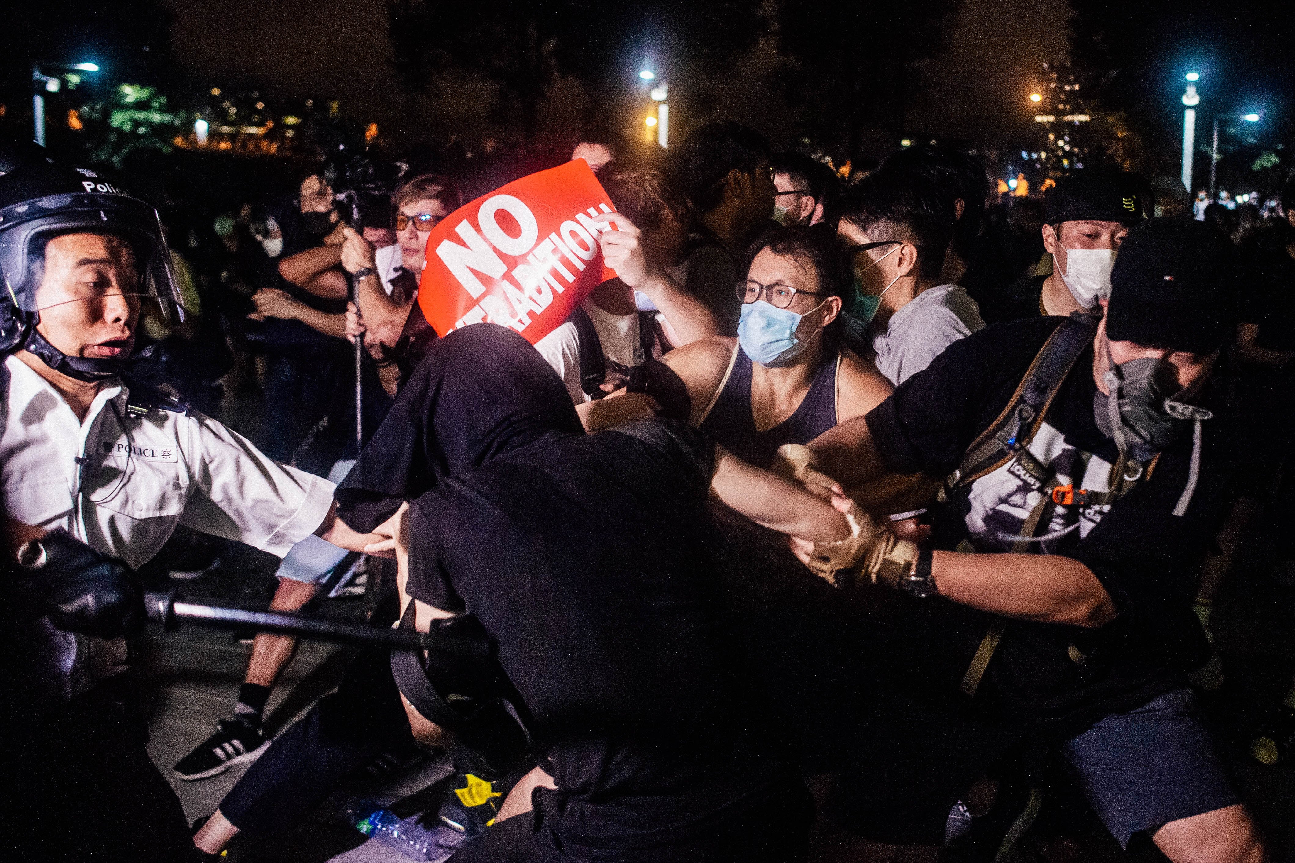 A protester holds a sign that says, "No extradition," amid a tussle with police.