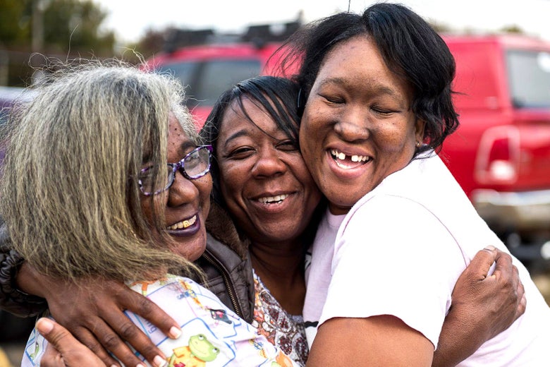 Three women hug one another.