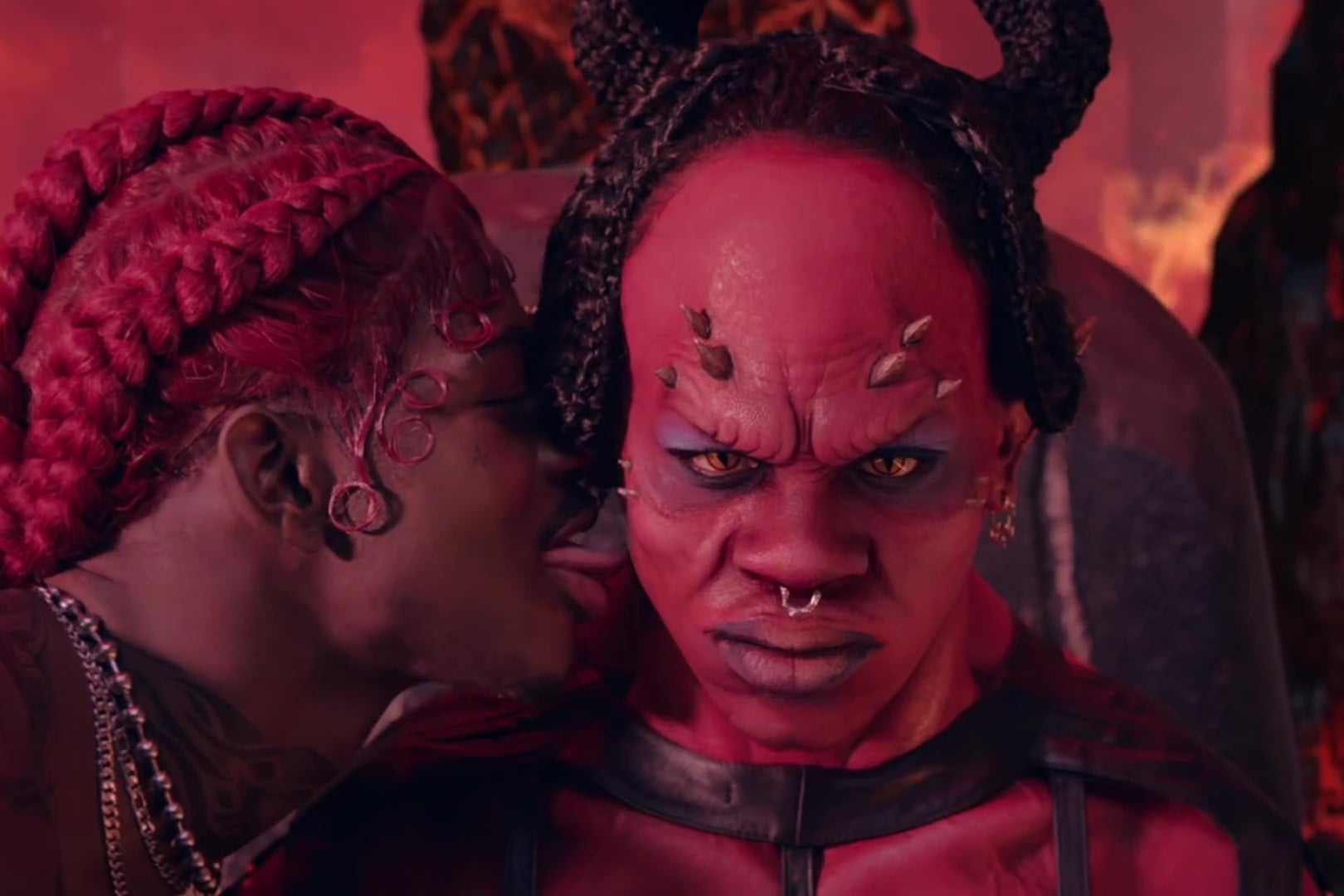 A closeup of Lil Nas X, in a red wig, licking Satan's face, in a still from his music video for Montero.