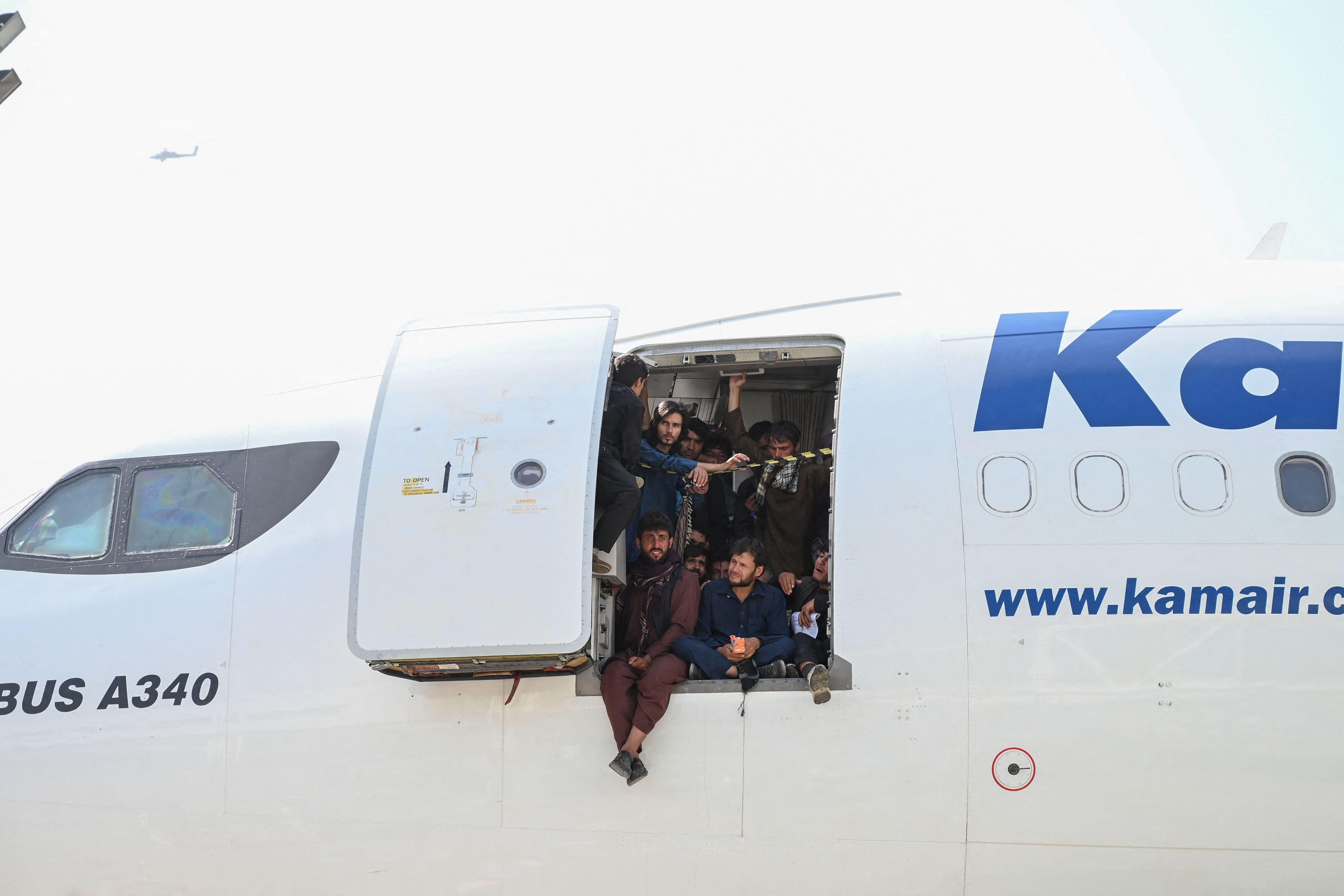 Afghan people climb up on a plane and sit by the door as they wait at the Kabul airport.