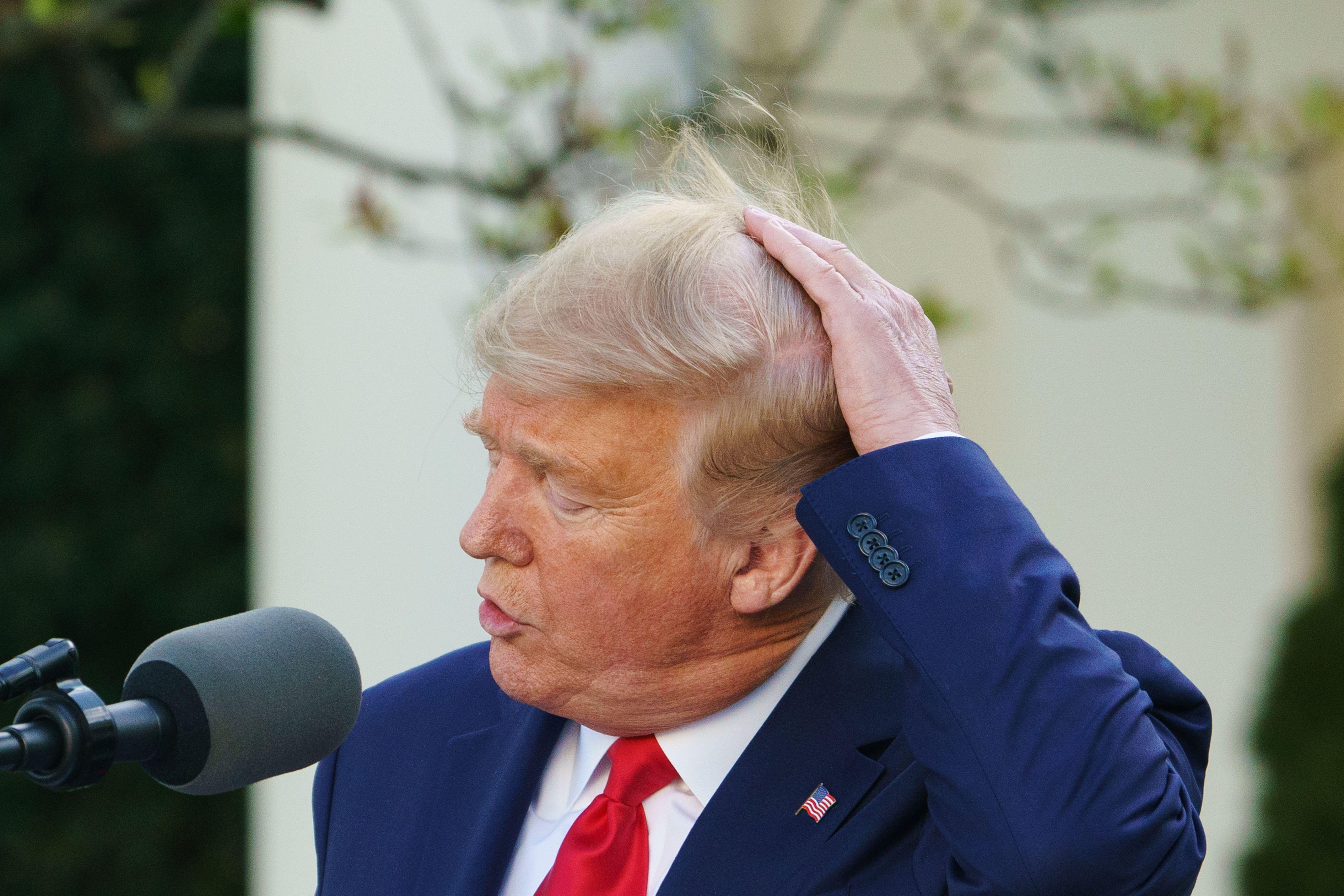 Trump pats down his hair while speaking into a microphone.