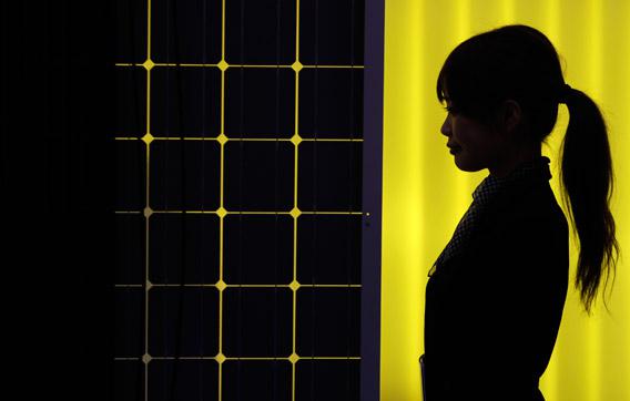 A woman is silhouetted next to a solar panel display by solar module supplier Upsolar at the International Photovoltaic Power Generation (PV) Expo in Tokyo, Japan.