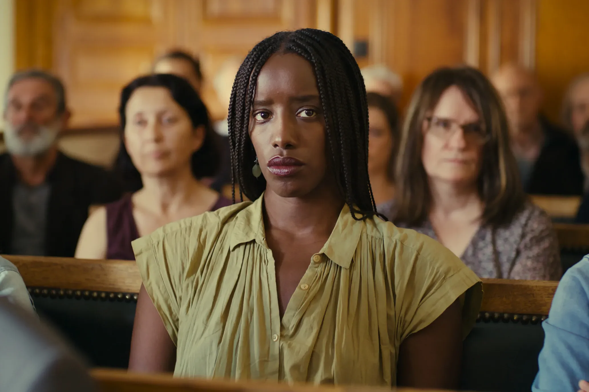 Kayije Kagame sits in a court room pew, looking at something ahead of her with a serious expression.