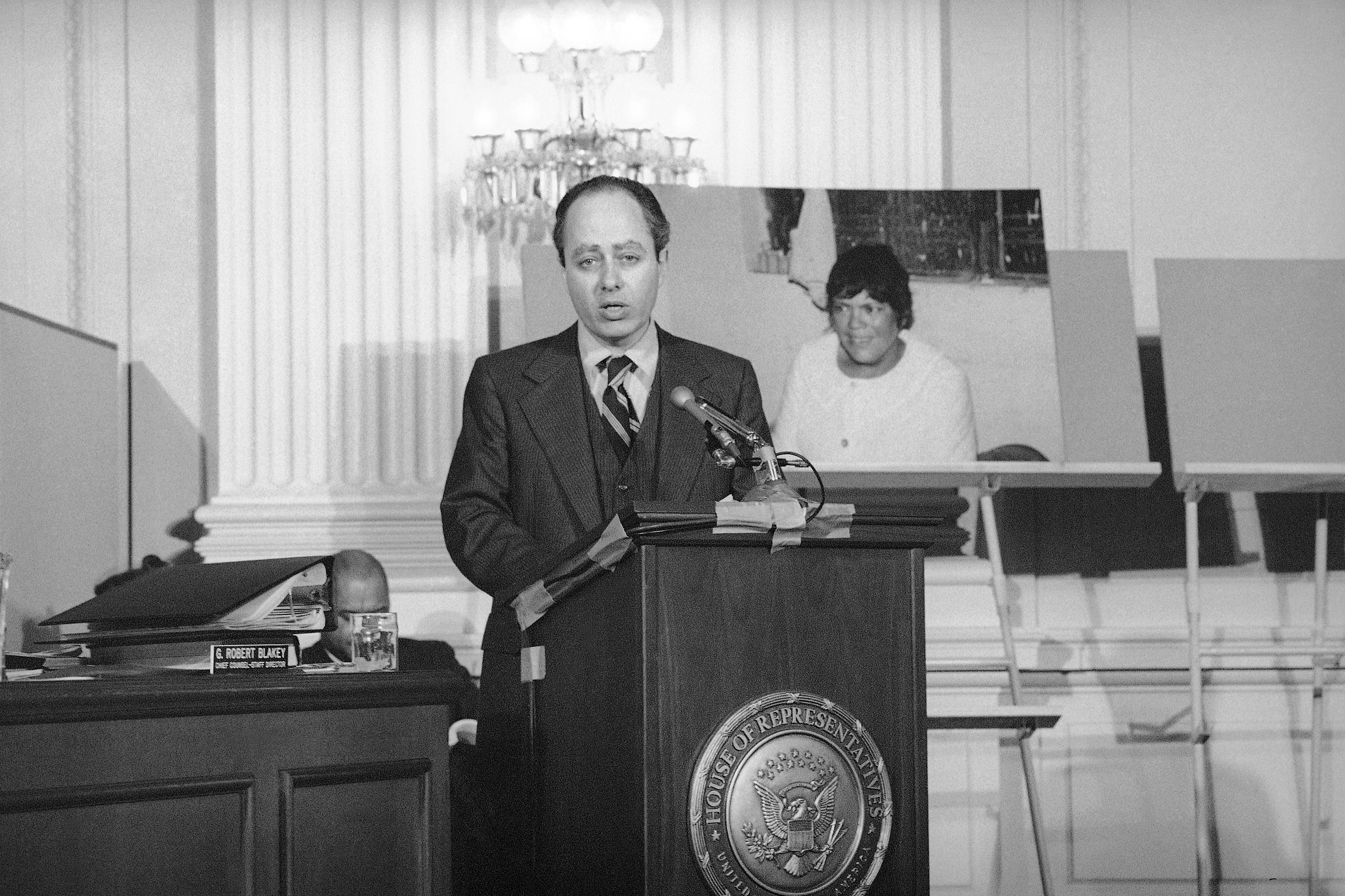 A balding middle-aged white man with dark hair stands behind a lectern in the House of Representatives and speaks into a microphone.