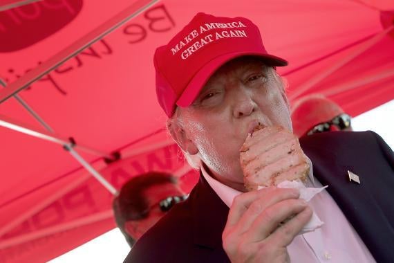 Donald Trump wears a MAGA hat and eats a pork chop on a stick. 