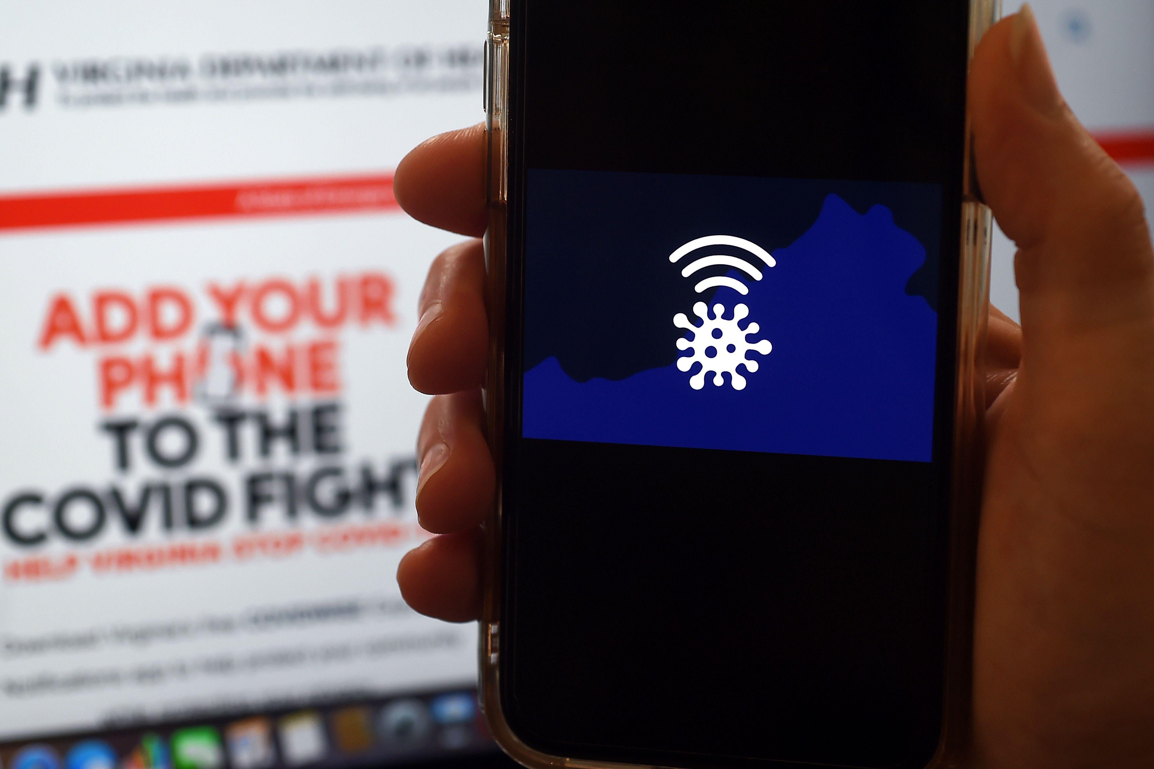 A hand holds a smartphone displaying the Covidwise app logo, while in the background a screen reads "Add your phone to the COVID fight."