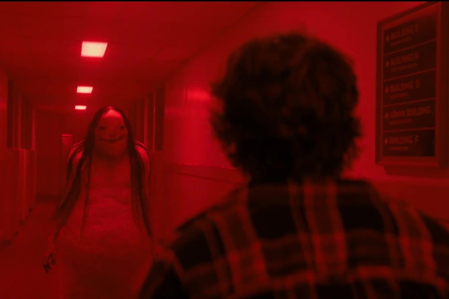 A ghastly, smiling, blob-like creature approaches a kid in a school hallway.