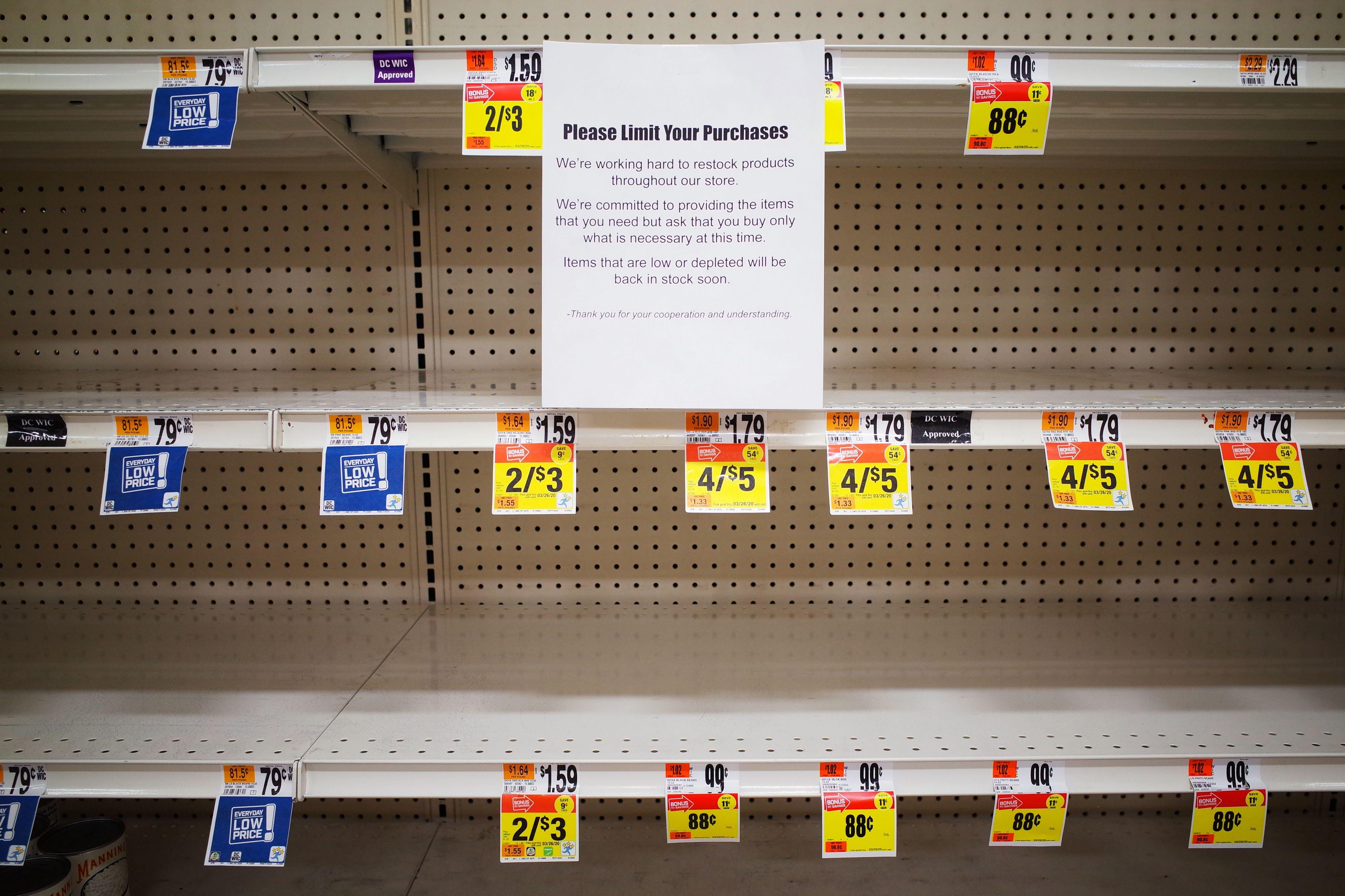 A message that says "Please limit your purchases" is posted on empty shelves for canned goods in a Giant supermarket.