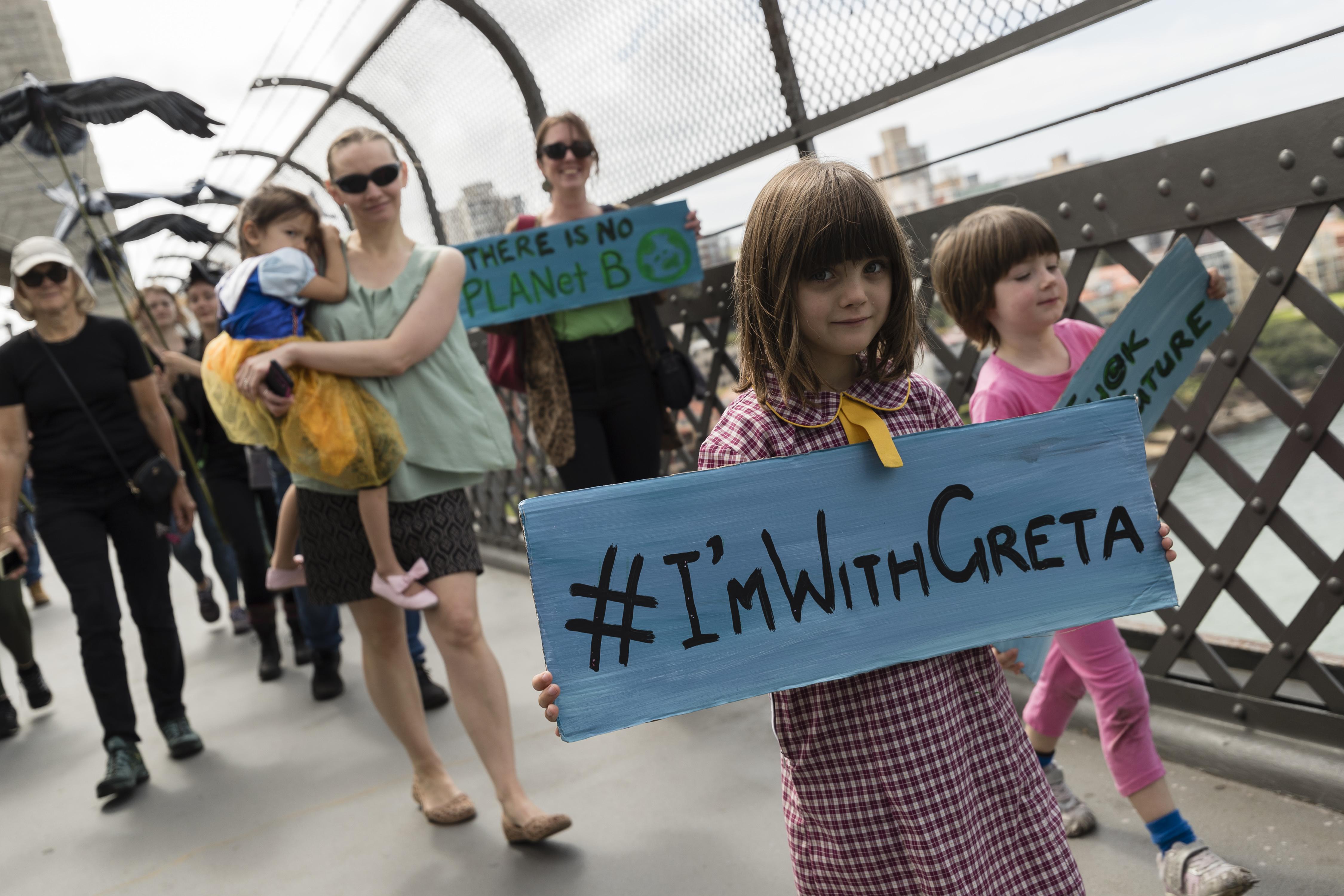 A young girl on a bridge holds a sign saying "#I'mWithGreta"