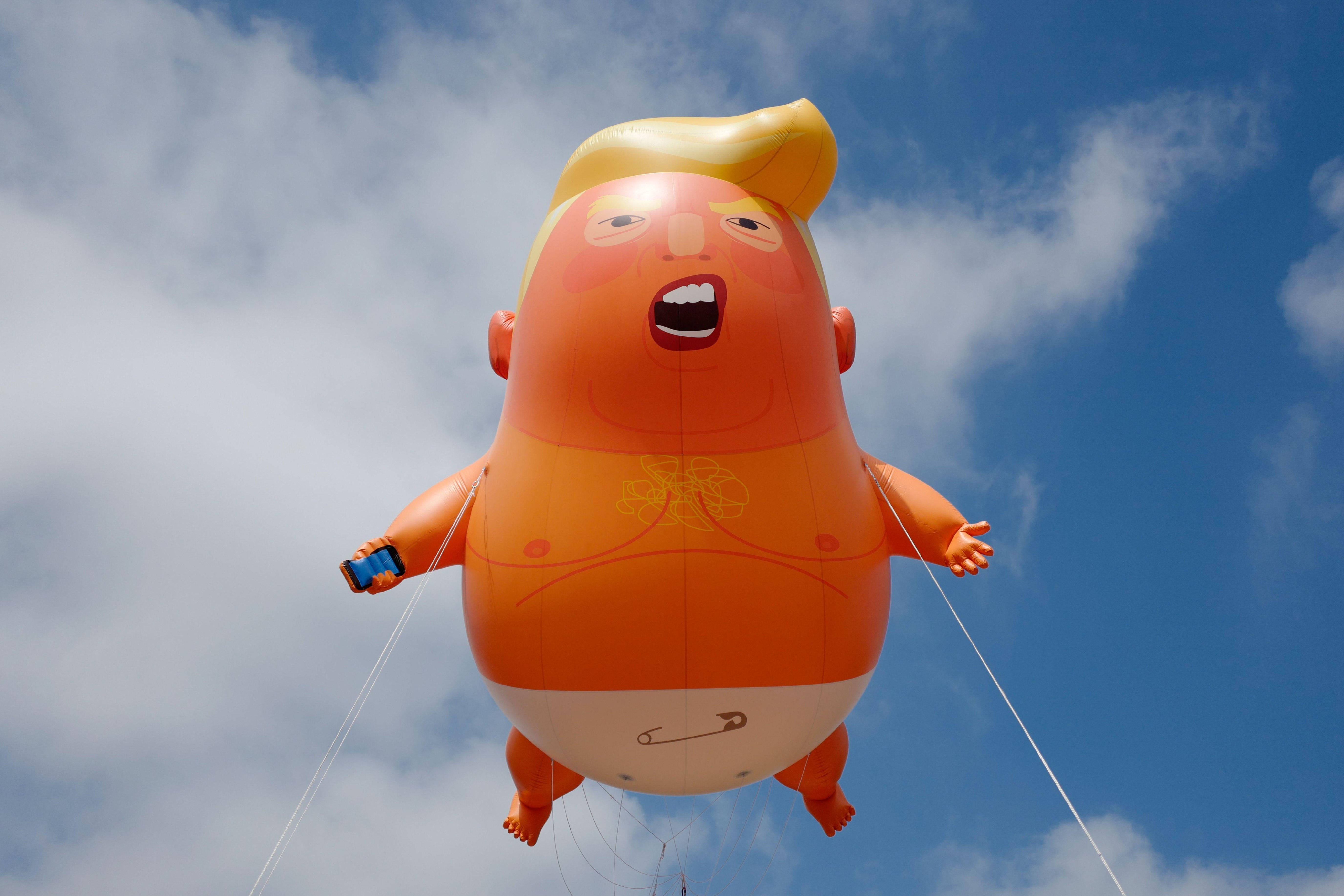 A giant balloon made to look like Donald Trump, with orange skin, yellow hair, a diaper, and a cellphone in its hand, floats in the sky.