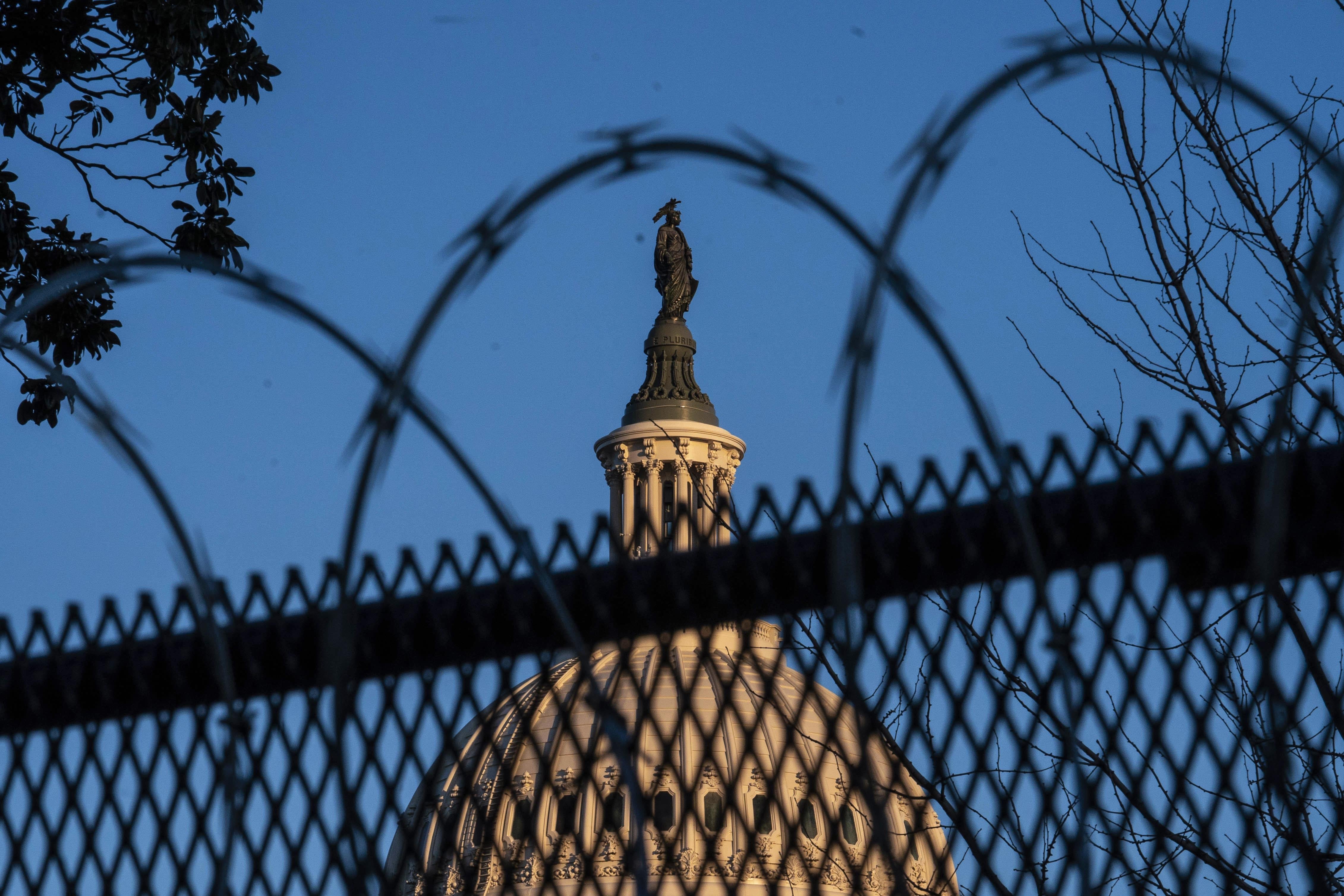 The top of the Capitol is seen through a barbed wire fence.
