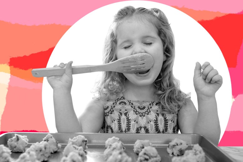 Jeune fille mangeant de la pâte à biscuits d'une cuillère en bois devant un plateau de biscuits.
