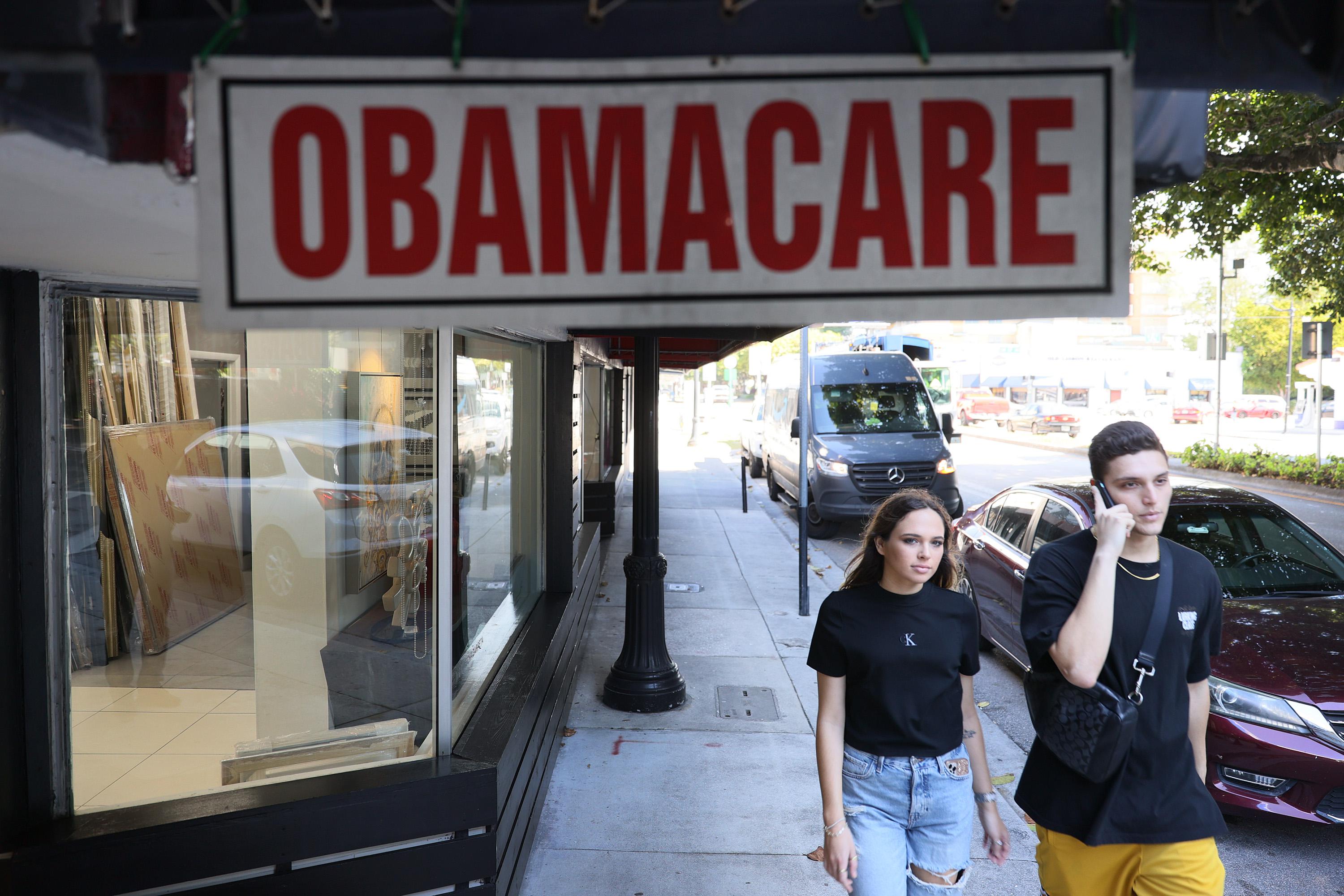 Two young people walk past an Obamacare sign hanging outside a storefront in Miami