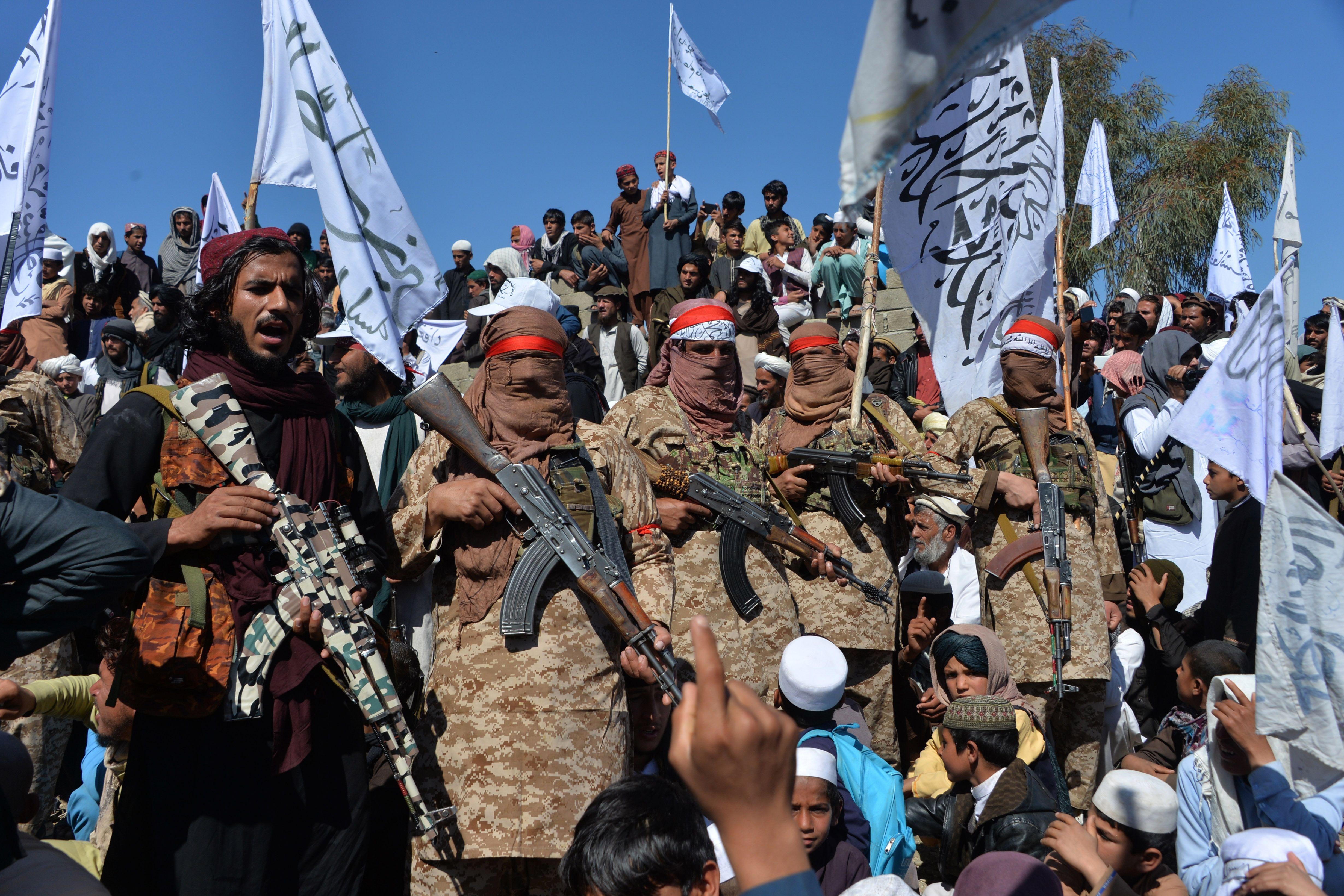 Afghan Taliban militants and villagers stand holding rifles and flags. 