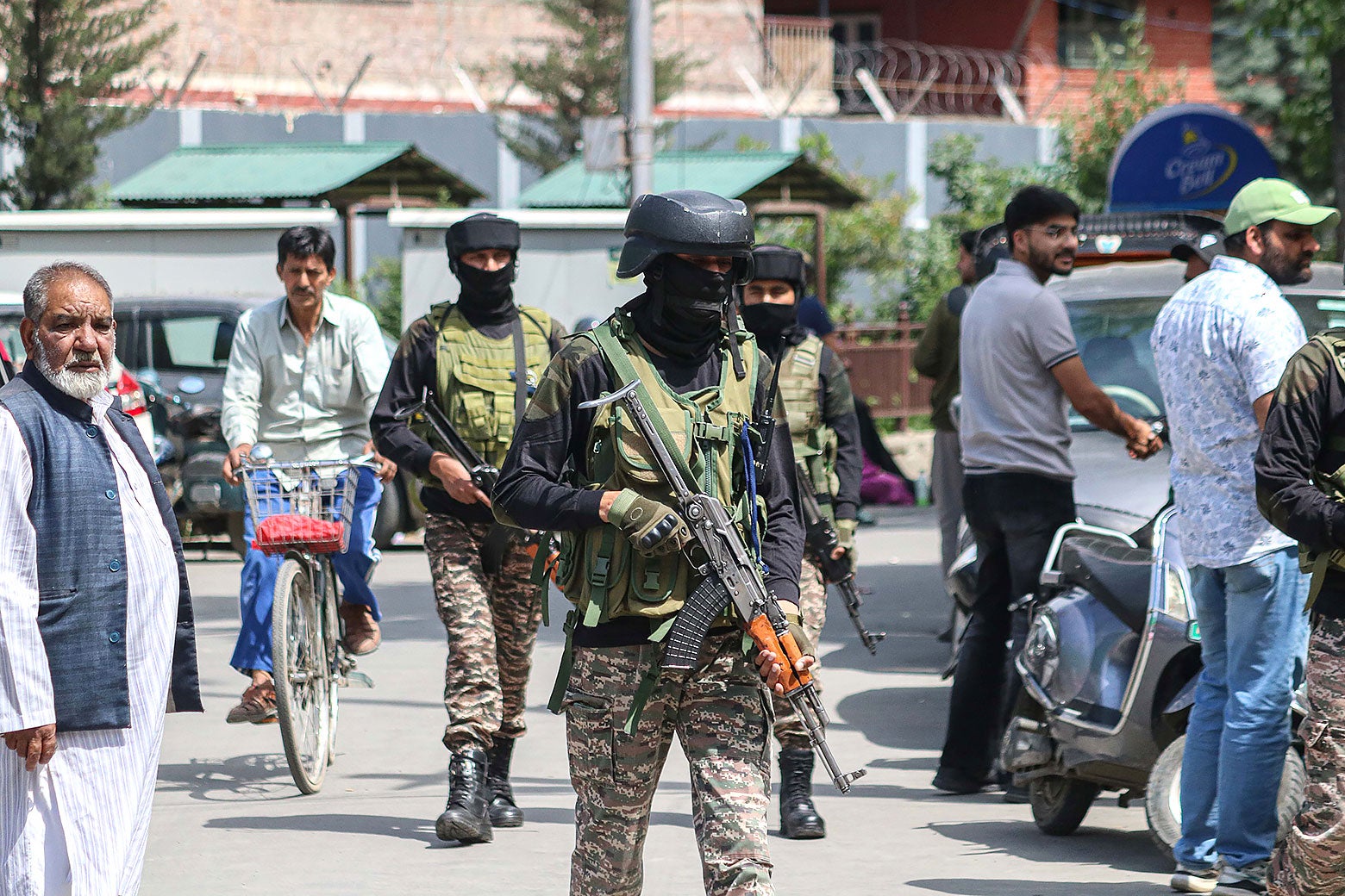 Soldiers in fatigues and face masks carrying guns walk through a street lined with people.