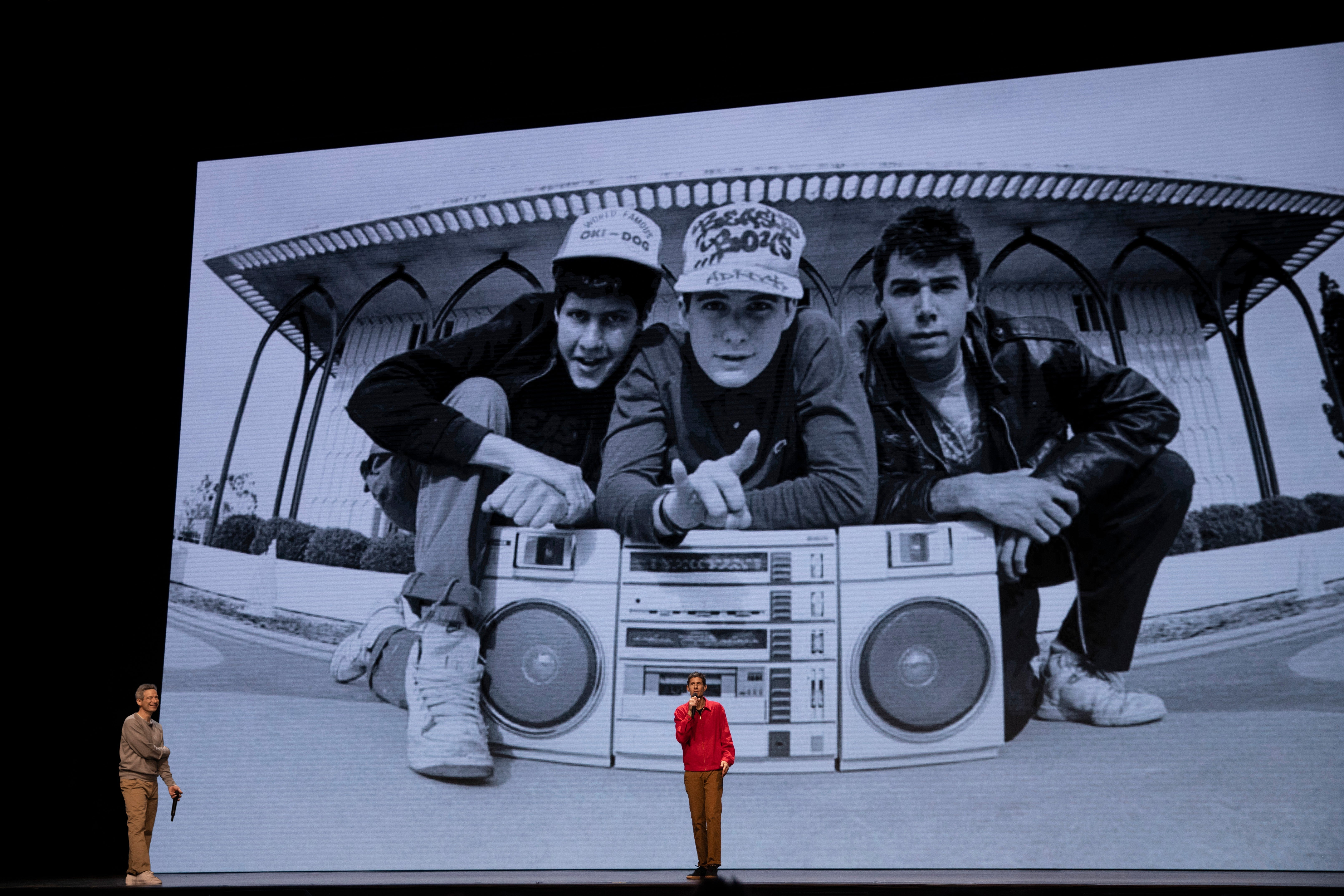 Ad-Rock and Mike D hold microphones onstage in front of a giant screen showing the three Beastie Boys gathered around a boombox in their youth