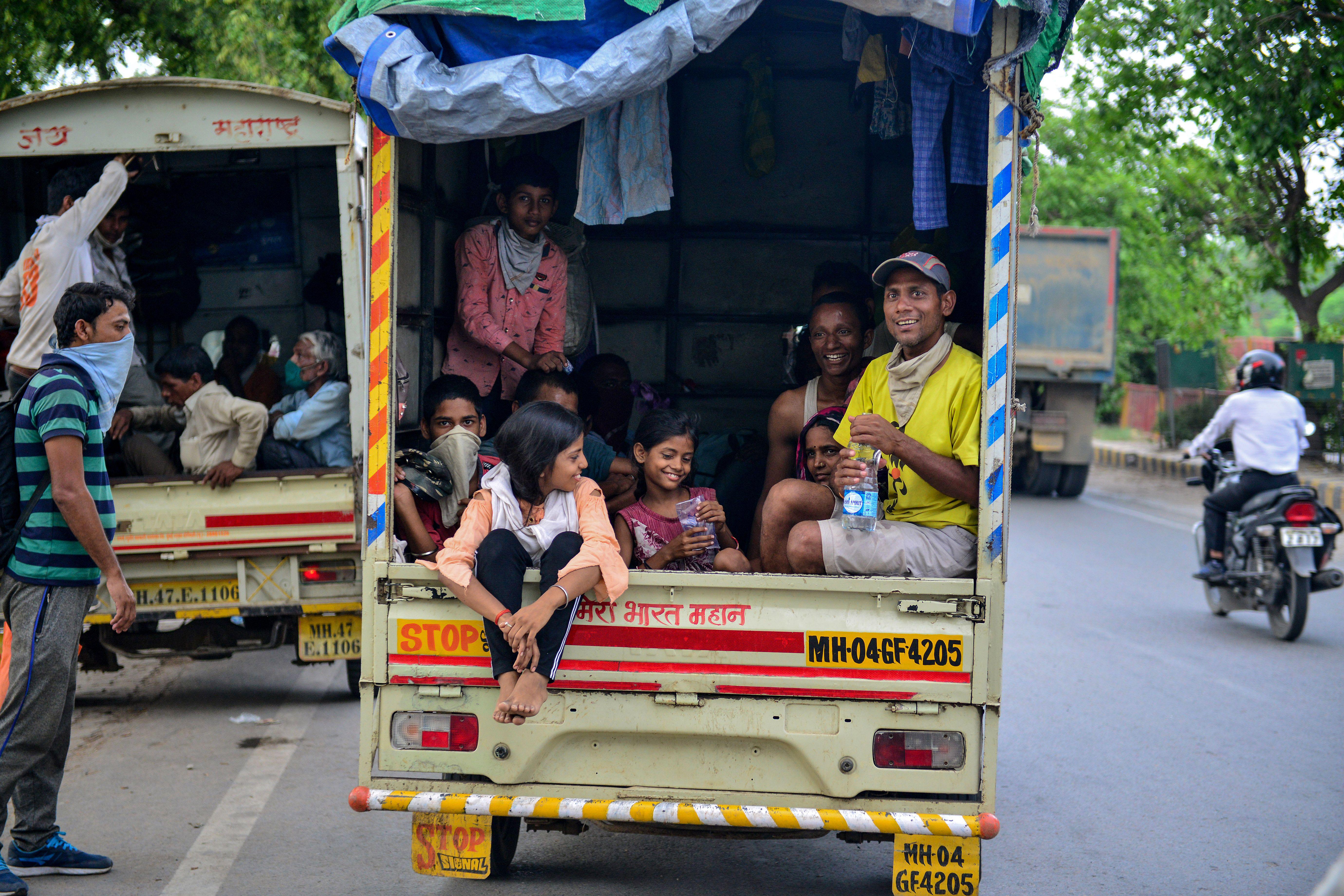 Adults and children, some wearing face coverings, sit in the back of a truck.